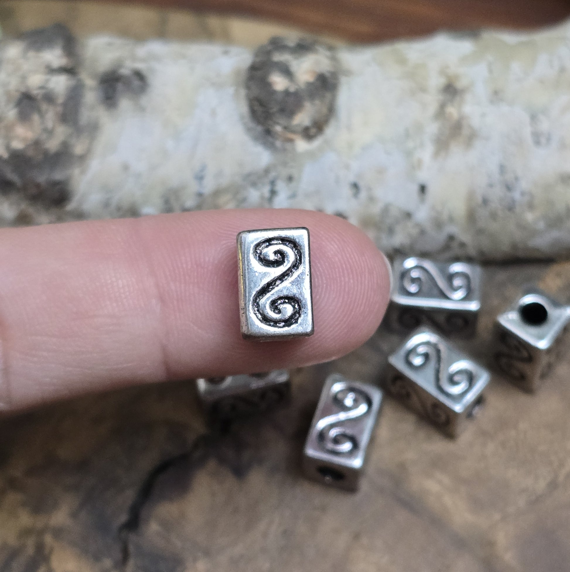 Eckige Metallperlen in Antiksilber mit S-förmigem Gravurmuster. Die strukturierte Oberfläche sorgt für einen eleganten Akzent. Mit einer Größe von 11 mm eignen sie sich perfekt für Armbänder, Ketten und kreative Schmuckdesigns.
