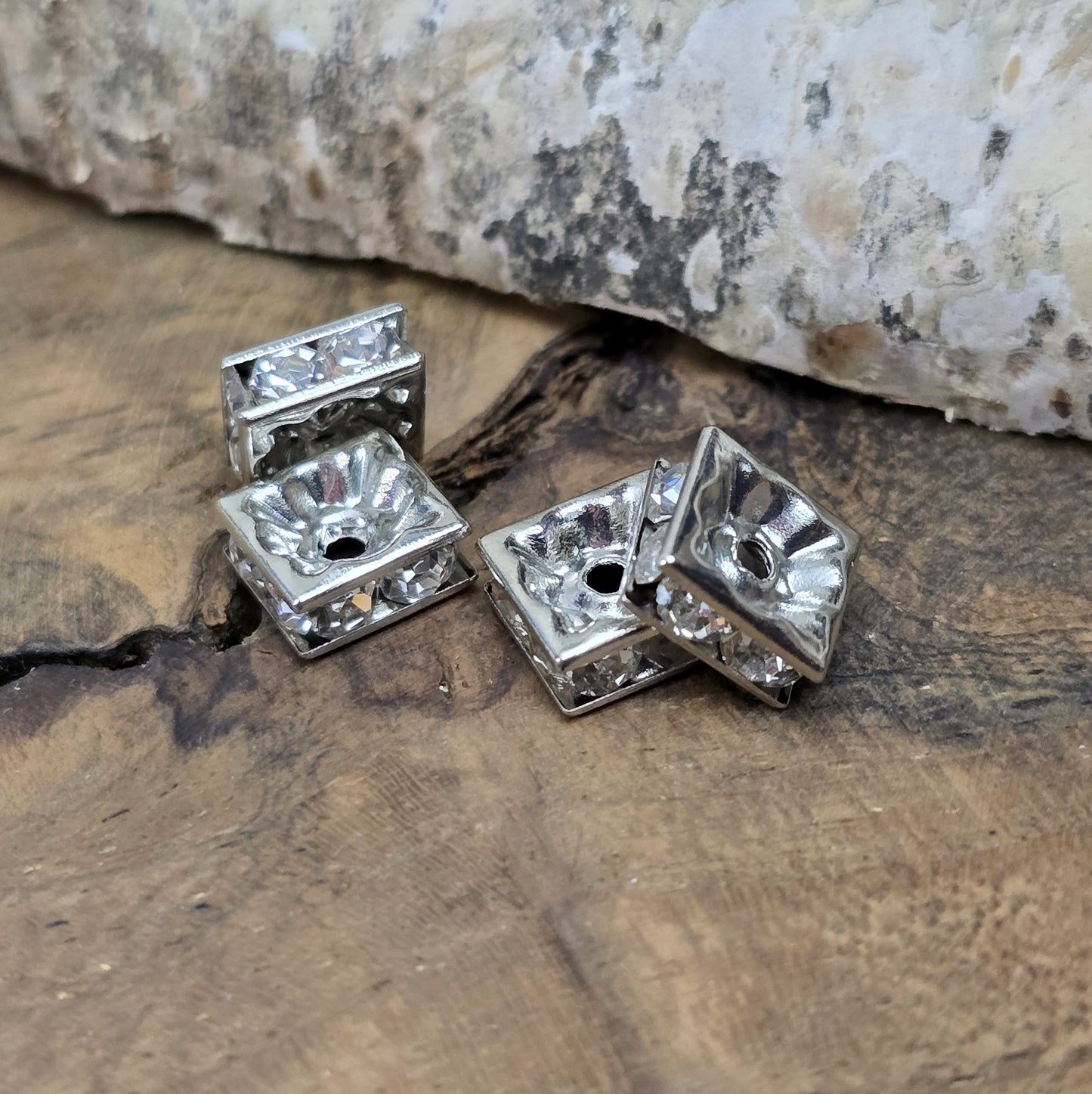 Vier eckige, silberfarbene Perlen mit funkelnden, klaren Strasssteinen aus Glas. Jede Seite der 8 x 8 mm großen Perle ist mit zwei Strasssteinen verziert. Perfekt für Armbänder, Ketten oder elegante Schmuckakzente. Fädelloch: 1,5 mm.
