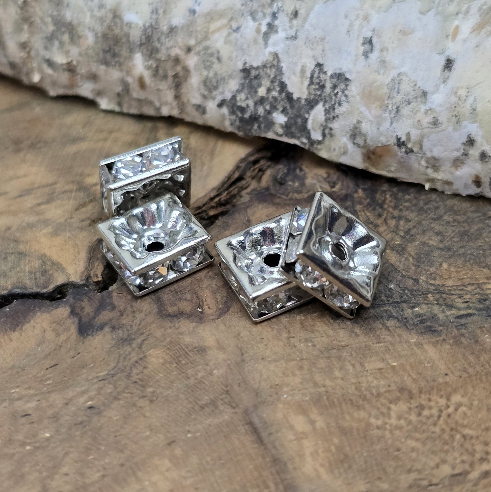 Vier eckige, silberfarbene Perlen mit funkelnden, klaren Strasssteinen aus Glas. Jede Seite der 8 x 8 mm großen Perle ist mit zwei Strasssteinen verziert. Perfekt für Armbänder, Ketten oder elegante Schmuckakzente. Fädelloch: 1,5 mm.