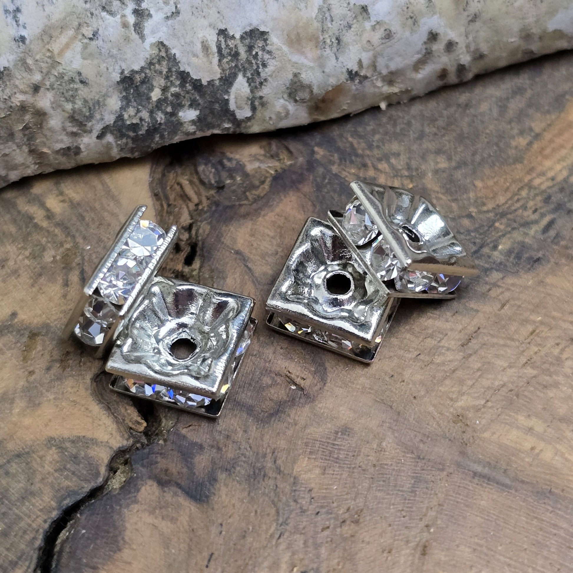 Vier eckige, silberfarbene Perlen mit funkelnden, klaren Strasssteinen aus Glas. Jede Seite der 8 x 8 mm großen Perle ist mit zwei Strasssteinen verziert. Perfekt für Armbänder, Ketten oder elegante Schmuckakzente. Fädelloch: 1,5 mm.
