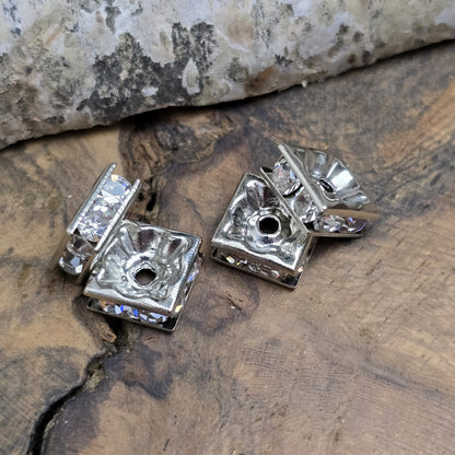 Vier eckige, silberfarbene Perlen mit funkelnden, klaren Strasssteinen aus Glas. Jede Seite der 8 x 8 mm großen Perle ist mit zwei Strasssteinen verziert. Perfekt für Armbänder, Ketten oder elegante Schmuckakzente. Fädelloch: 1,5 mm.