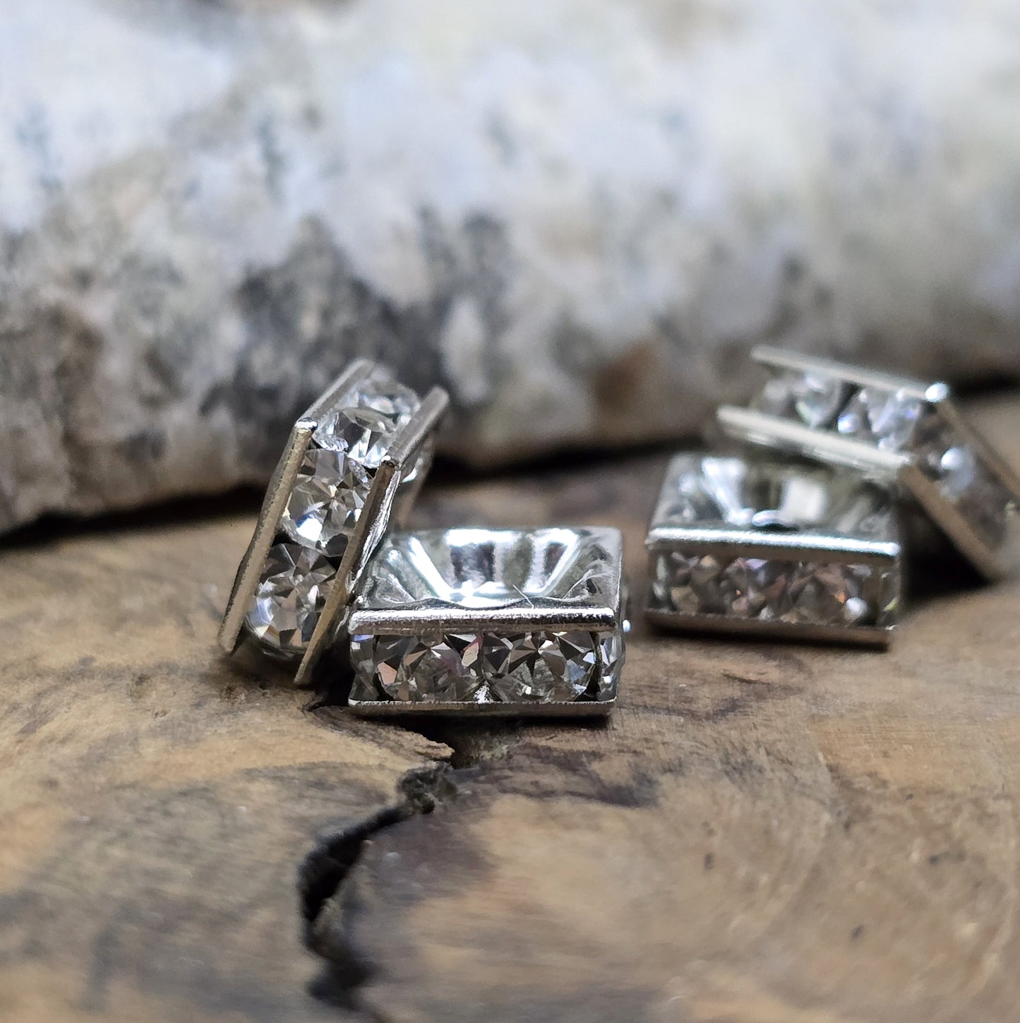 Vier eckige, silberfarbene Perlen mit funkelnden, klaren Strasssteinen aus Glas. Jede Seite der 8 x 8 mm großen Perle ist mit zwei Strasssteinen verziert. Perfekt für Armbänder, Ketten oder elegante Schmuckakzente. Fädelloch: 1,5 mm.