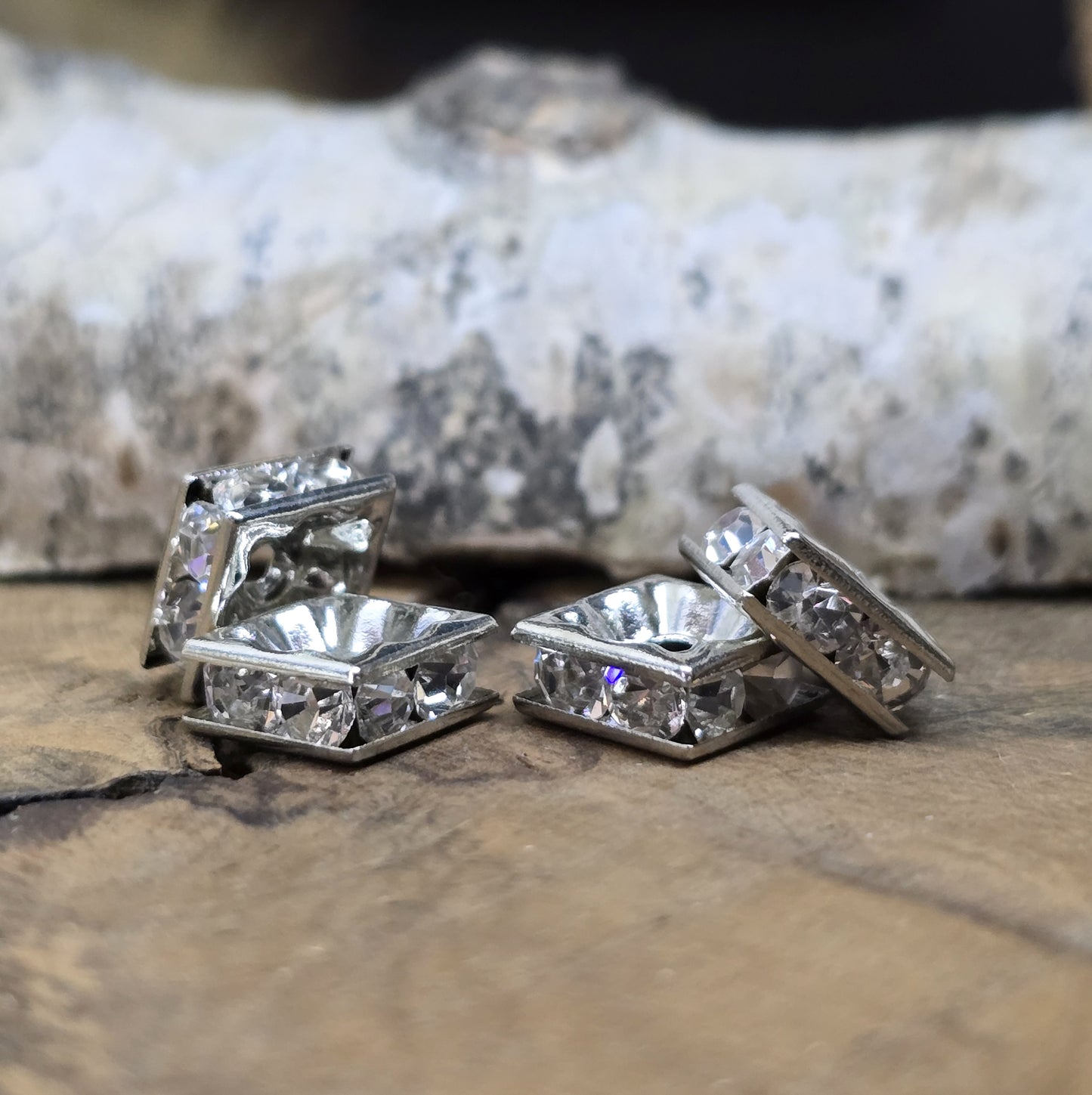 Vier eckige, silberfarbene Perlen mit funkelnden, klaren Strasssteinen aus Glas. Jede Seite der 8 x 8 mm großen Perle ist mit zwei Strasssteinen verziert. Perfekt für Armbänder, Ketten oder elegante Schmuckakzente. Fädelloch: 1,5 mm.