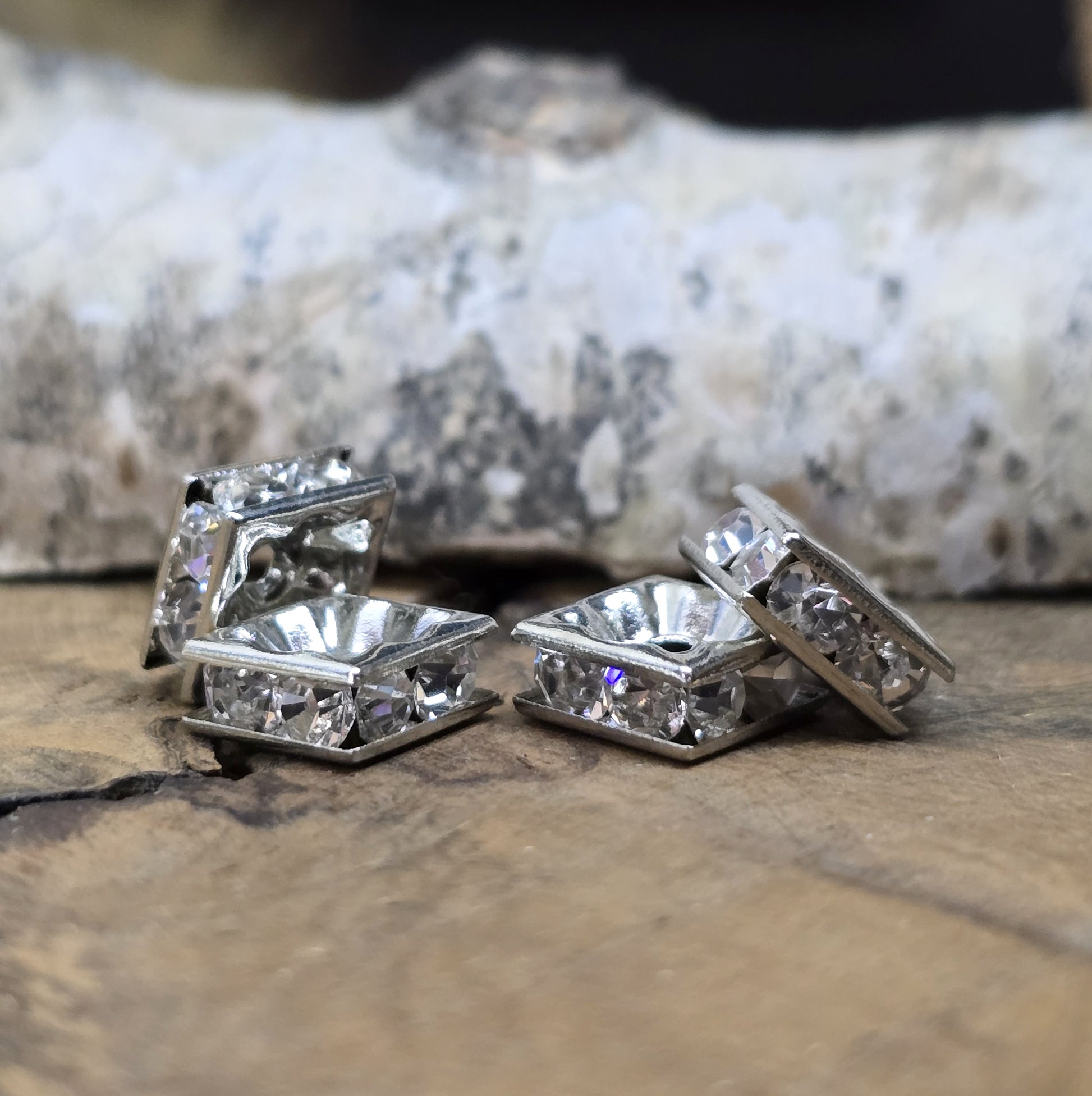 Vier eckige, silberfarbene Perlen mit funkelnden, klaren Strasssteinen aus Glas. Jede Seite der 8 x 8 mm großen Perle ist mit zwei Strasssteinen verziert. Perfekt für Armbänder, Ketten oder elegante Schmuckakzente. Fädelloch: 1,5 mm.