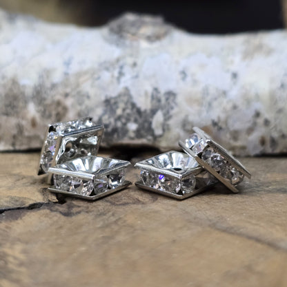 Vier eckige, silberfarbene Perlen mit funkelnden, klaren Strasssteinen aus Glas. Jede Seite der 8 x 8 mm großen Perle ist mit zwei Strasssteinen verziert. Perfekt für Armbänder, Ketten oder elegante Schmuckakzente. Fädelloch: 1,5 mm.