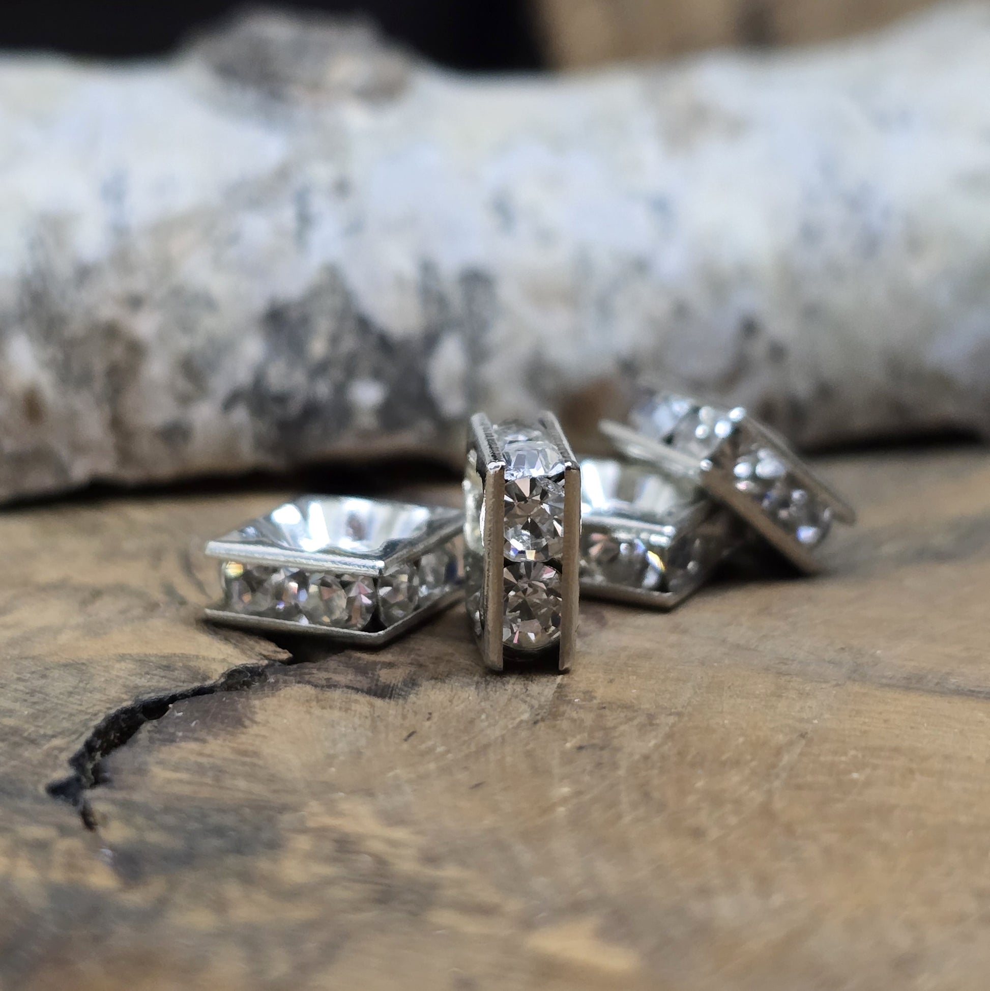 Vier eckige, silberfarbene Perlen mit funkelnden, klaren Strasssteinen aus Glas. Jede Seite der 8 x 8 mm großen Perle ist mit zwei Strasssteinen verziert. Perfekt für Armbänder, Ketten oder elegante Schmuckakzente. Fädelloch: 1,5 mm.