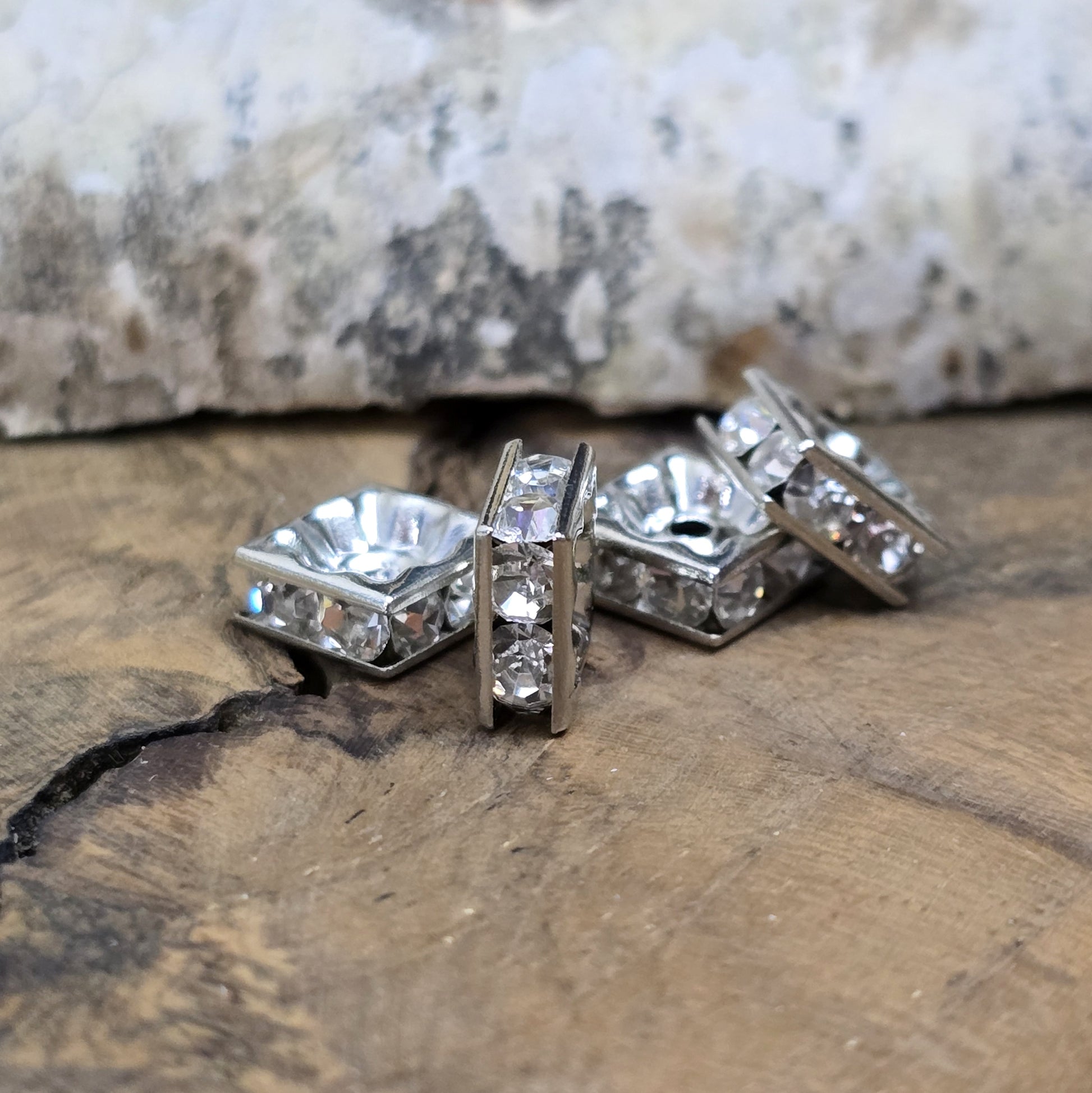Vier eckige, silberfarbene Perlen mit funkelnden, klaren Strasssteinen aus Glas. Jede Seite der 8 x 8 mm großen Perle ist mit zwei Strasssteinen verziert. Perfekt für Armbänder, Ketten oder elegante Schmuckakzente. Fädelloch: 1,5 mm.