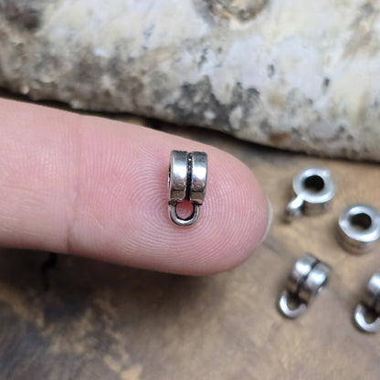 Das Bild zeigt antiksilberfarbene Metallperlen mit Öse. Sie sind eine ideale Ergänzung für kreative Schmuckprojekte. Dank des großzügigen 3-mm-Lochs lassen sie sich mühelos auf verschiedene Bänder und Kordeln auffädeln. Die zusätzliche Öse eröffnet zahlreiche Designmöglichkeiten, um Schmuckstücke individuell zu gestalten.