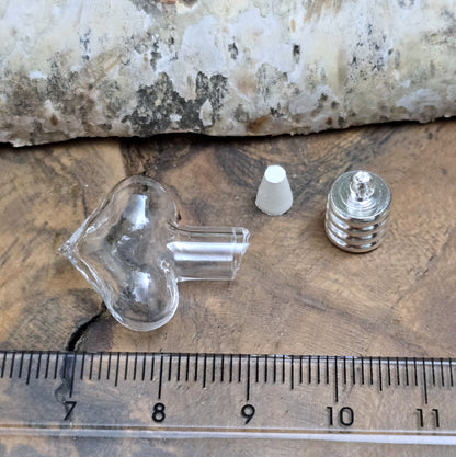 Kleiner Phiolenanhänger aus Glas, in Form eines Herzens mit silberfarbiger Kappe. Ideal zum Befüllen mit beschriftetem Reiskorn, Sand, Milchzahn, Asche, Haare udg.