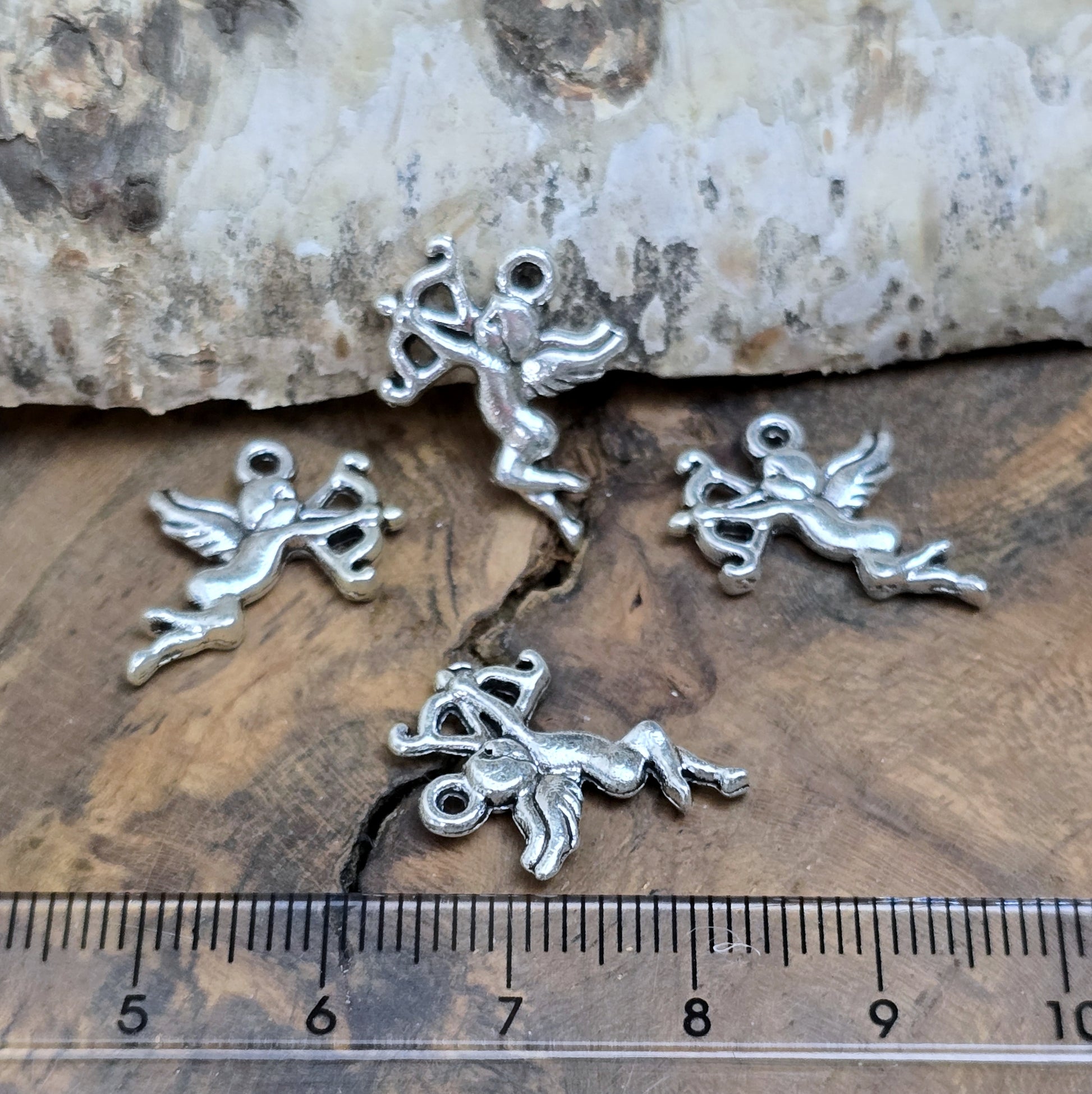 4 Charms Armor in antik silberfarbig liegend auf einem Holzbrett mit einem Lineal für einen besseren Größenvergleich