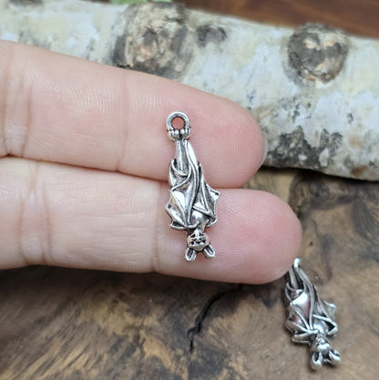 2 antik silberne Charms, hängende Fledermaus in Detailansicht, auf zwei Fingern liegend für bessere Größenreferenz