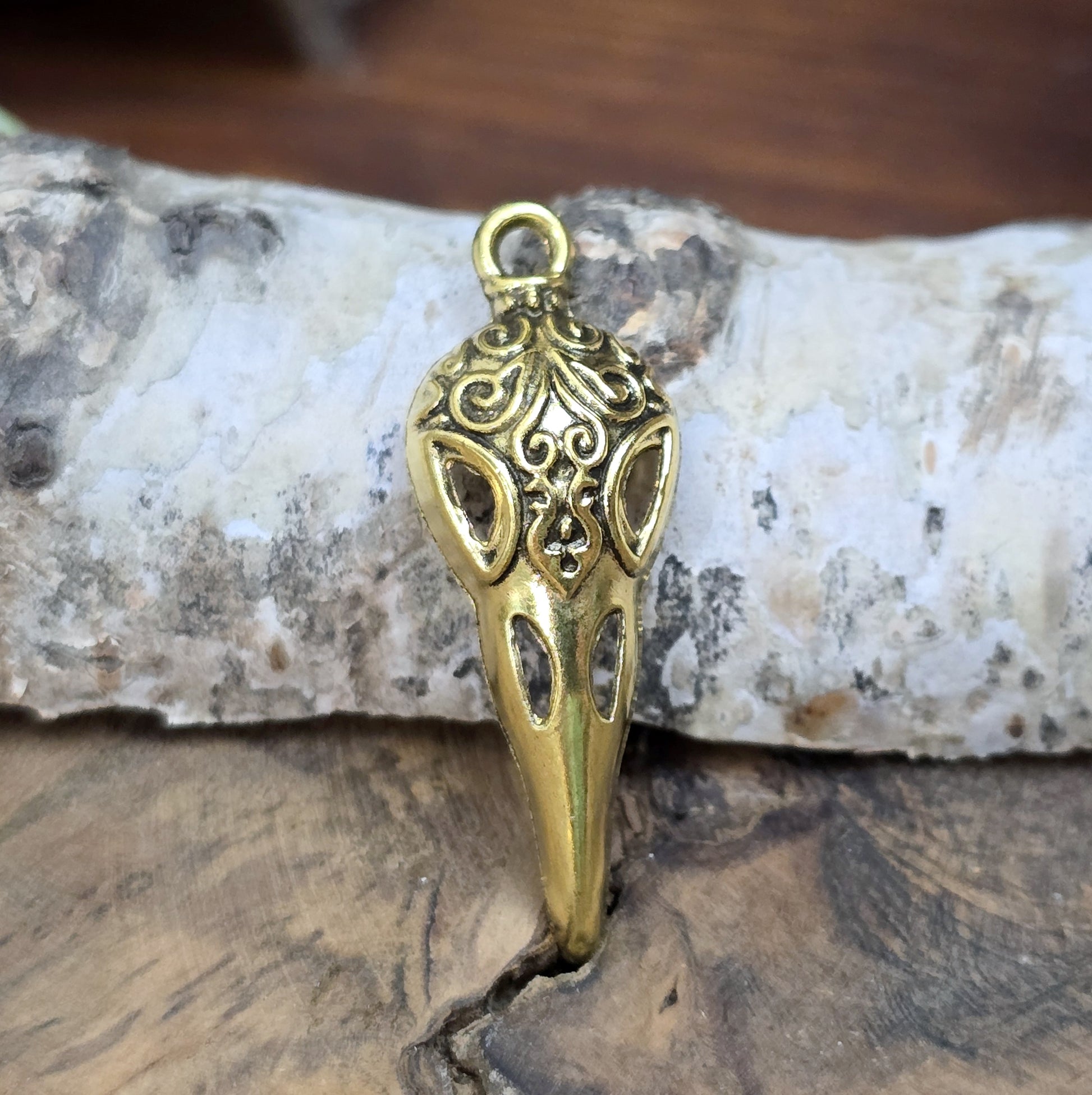 Das Bild zeigt einen detaillierten Krähenschädel mit Intarsien, gehalten in antik goldfarbenem Finish. Er ist einseitig geprägt und hat eine hohle Rückseite, was ihn leicht und vielseitig macht.