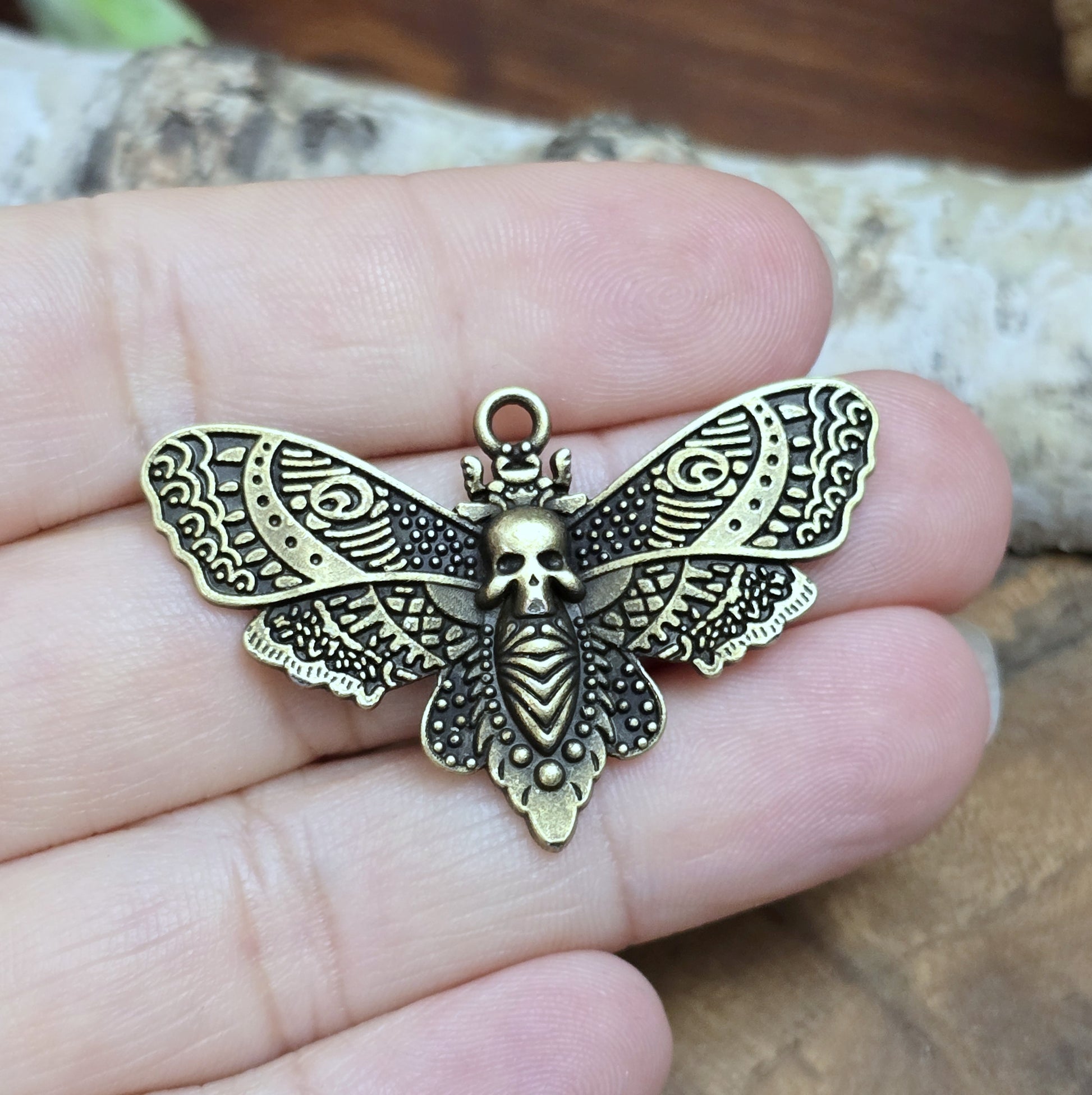 Das Bild zeigt einen Anhänger im antik bronzefarbenen Look. Mit einer Breite von 27 mm und einer stabilen Öse eignet er sich perfekt für die Gestaltung von Ketten, Chokern oder anderen individuellen Schmuckstücken.
