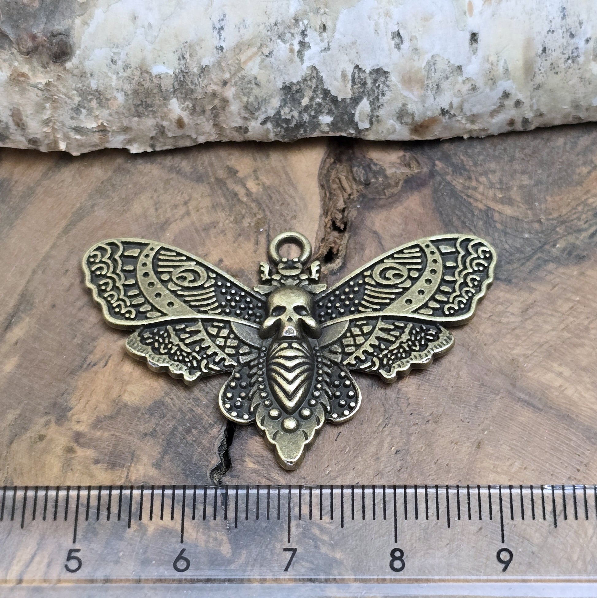 Das Bild zeigt einen Anhänger im antik bronzefarbenen Look. Mit einer Breite von 27 mm und einer stabilen Öse eignet er sich perfekt für die Gestaltung von Ketten, Chokern oder anderen individuellen Schmuckstücken.
