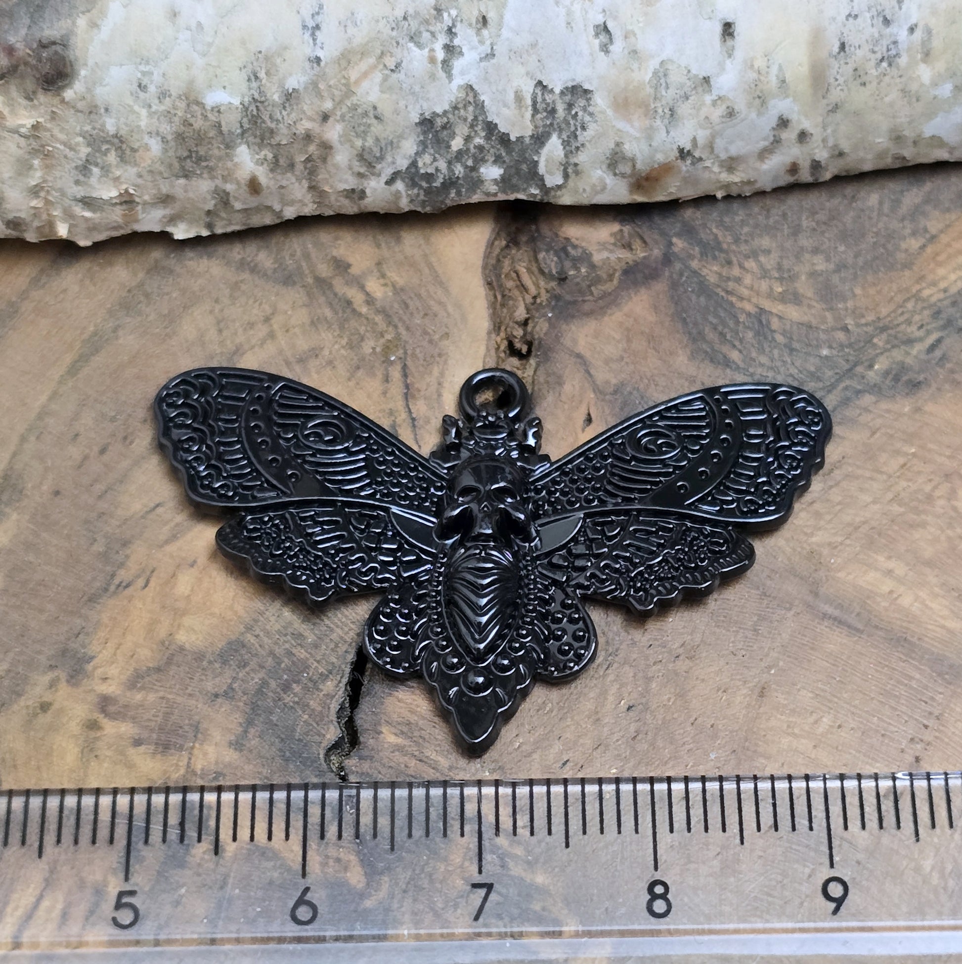 Das Bild zeigt einen Anhänger mit schwarzer Beschichtung. Mit 27 mm Breite und einer stabilen Öse eignet er sich perfekt für Ketten, Choker und andere individuelle Schmuckstücke.