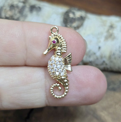 Das Bild zeigt einen eleganten Charms-Anhänger aus Messing, veredelt mit 24 Karat Vergoldung und funkelnden Strasssteinen. Das Seepferdchen, Symbol für Anmut und das Meer, wird hier in seiner ganzen Schönheit hervorgehoben.