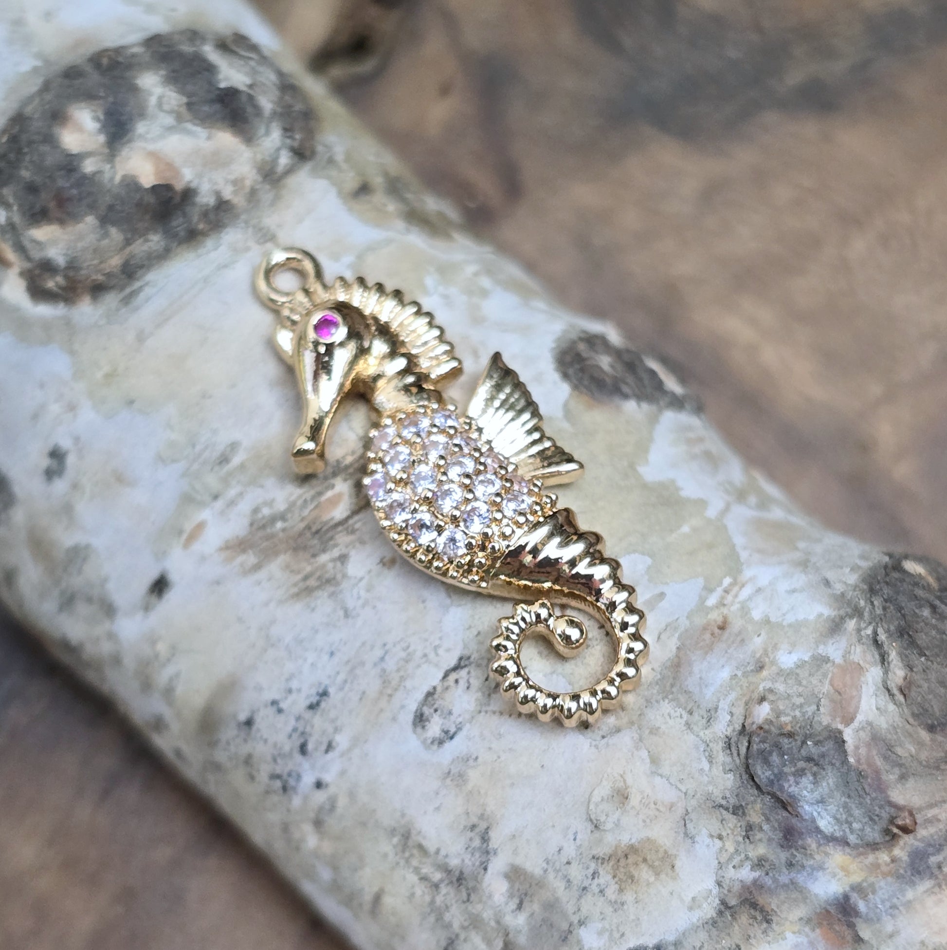 Das Bild zeigt einen eleganten Charms-Anhänger aus Messing, veredelt mit 24 Karat Vergoldung und funkelnden Strasssteinen. Das Seepferdchen, Symbol für Anmut und das Meer, wird hier in seiner ganzen Schönheit hervorgehoben.