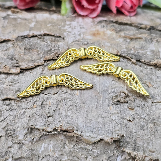 Das Bild zeigt mehrere vergoldete Flügelperlen aus Metall, jeweils 30 mm breit. Die Flügel sind filigran gestaltet, mit geschwungenen Linien und feinen Details. Sie eignen sich ideal zur Herstellung von Schutzengeln für Schmuck, Schlüsselanhänger oder Dekorationen. Die glänzende Goldfarbe verleiht ihnen eine edle und elegante Optik.