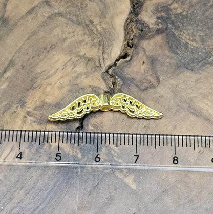 Das Bild zeigt mehrere vergoldete Flügelperlen aus Metall, jeweils 30 mm breit. Die Flügel sind filigran gestaltet, mit geschwungenen Linien und feinen Details. Sie eignen sich ideal zur Herstellung von Schutzengeln für Schmuck, Schlüsselanhänger oder Dekorationen. Die glänzende Goldfarbe verleiht ihnen eine edle und elegante Optik.