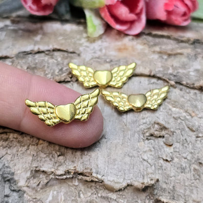Das Bild zeigt vergoldete Metallperlen in Form von Engelsflügeln mit einem Herz in der Mitte. Die Perlen sind 22 mm groß und eignen sich für die Herstellung von Schutzengel-Anhängern oder für DIY-Schmuckprojekte. Sie haben eine glänzende, goldene Oberfläche und ein elegantes Design.