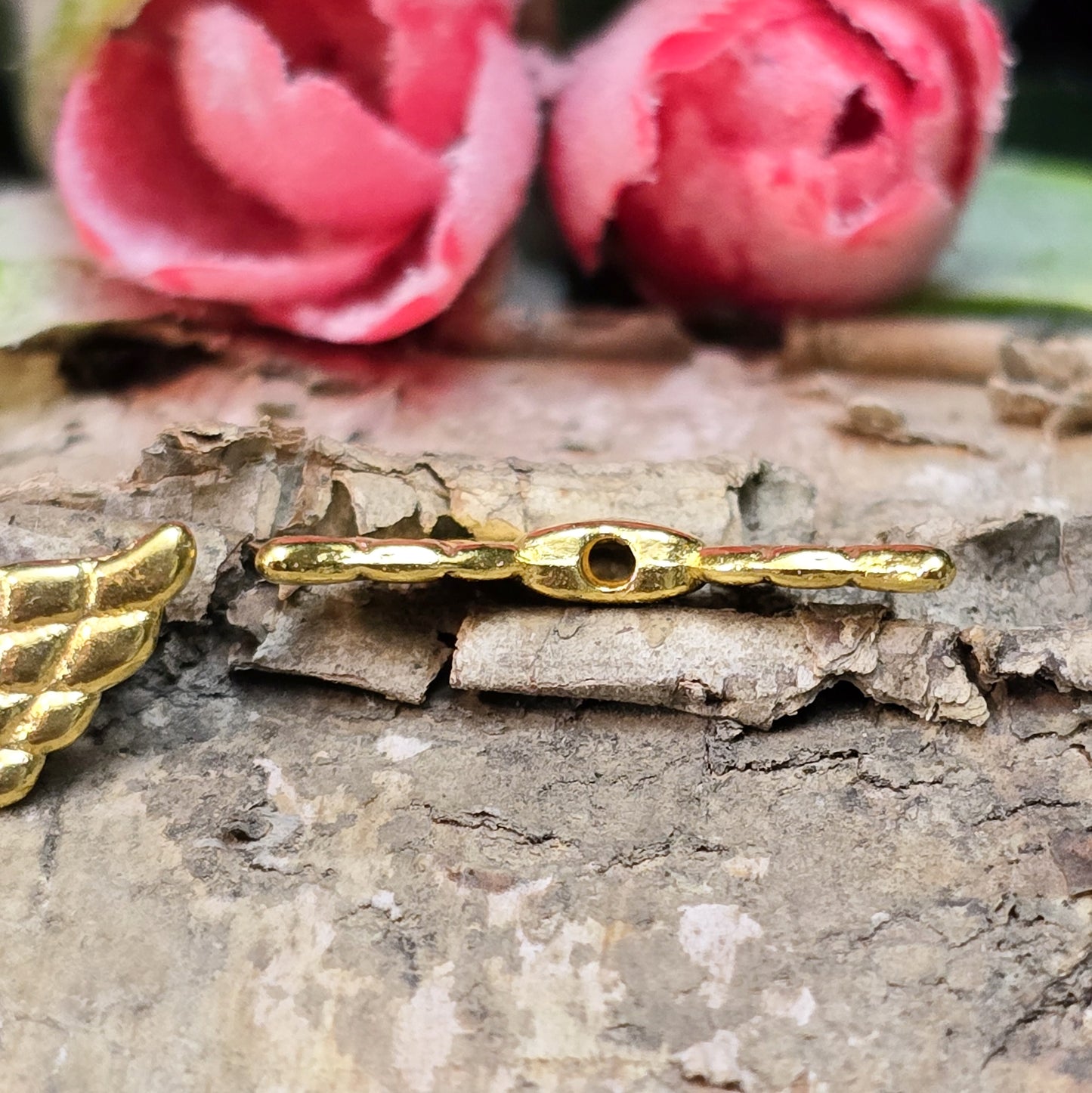 Das Bild zeigt vergoldete Metallperlen in Form von Engelsflügeln mit einem Herz in der Mitte. Die Perlen sind 22 mm groß und eignen sich für die Herstellung von Schutzengel-Anhängern oder für DIY-Schmuckprojekte. Sie haben eine glänzende, goldene Oberfläche und ein elegantes Design.