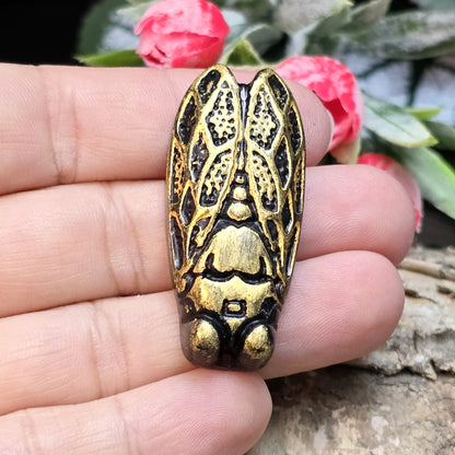 Das Bild zeigt einen handgefertigten Zikaden-Cabochon aus Kunstharz in einer edlen Bronze-Optik. Die Zikade hat eine flache Rückseite mit einem kleinen Loch zwischen den Augen, ideal für die Anbringung einer Anhängeröse.