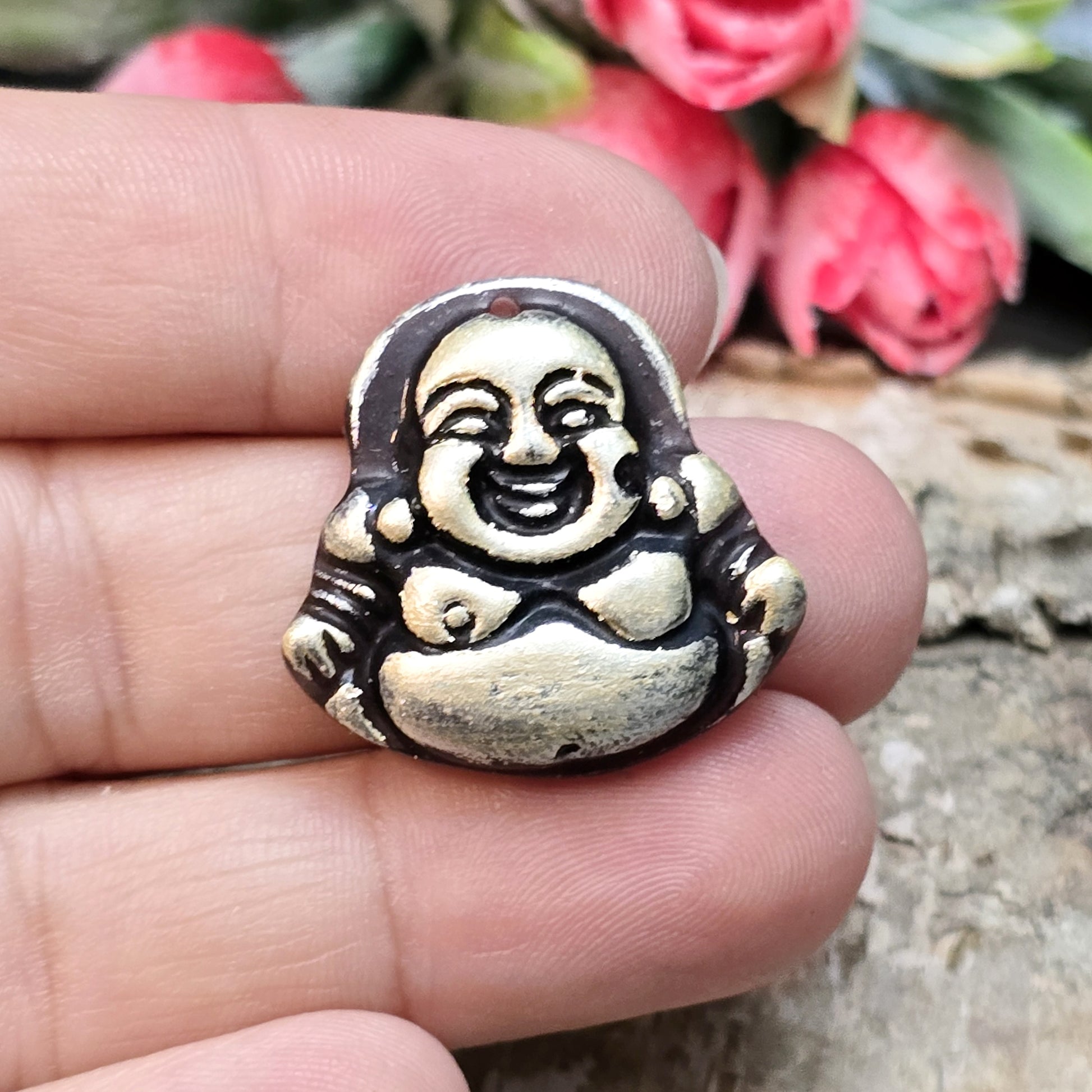 Das Bild zeigt einen handgefertigten Anhänger in Form eines lachenden Buddhas, gefertigt aus schwarzem Kunstharz mit roségoldenen Details. Der Buddha hat eine flache Rückseite und ein kleines Loch im oberen Bereich für eine Anhängeröse. Der Anhänger eignet sich hervorragend für Schmuckkreationen, Bastelprojekte oder zum Verzieren von Dekorationen.
