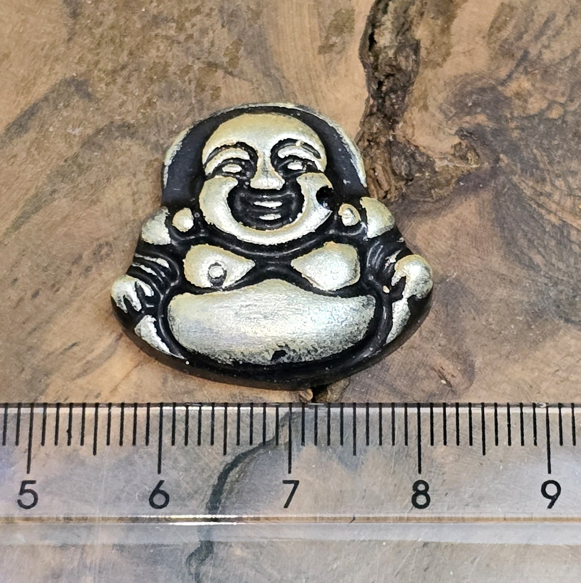 Das Bild zeigt einen handgefertigten Anhänger in Form eines lachenden Buddhas, gefertigt aus schwarzem Kunstharz mit roségoldenen Details. Der Buddha hat eine flache Rückseite und ein kleines Loch im oberen Bereich für eine Anhängeröse. Der Anhänger eignet sich hervorragend für Schmuckkreationen, Bastelprojekte oder zum Verzieren von Dekorationen.