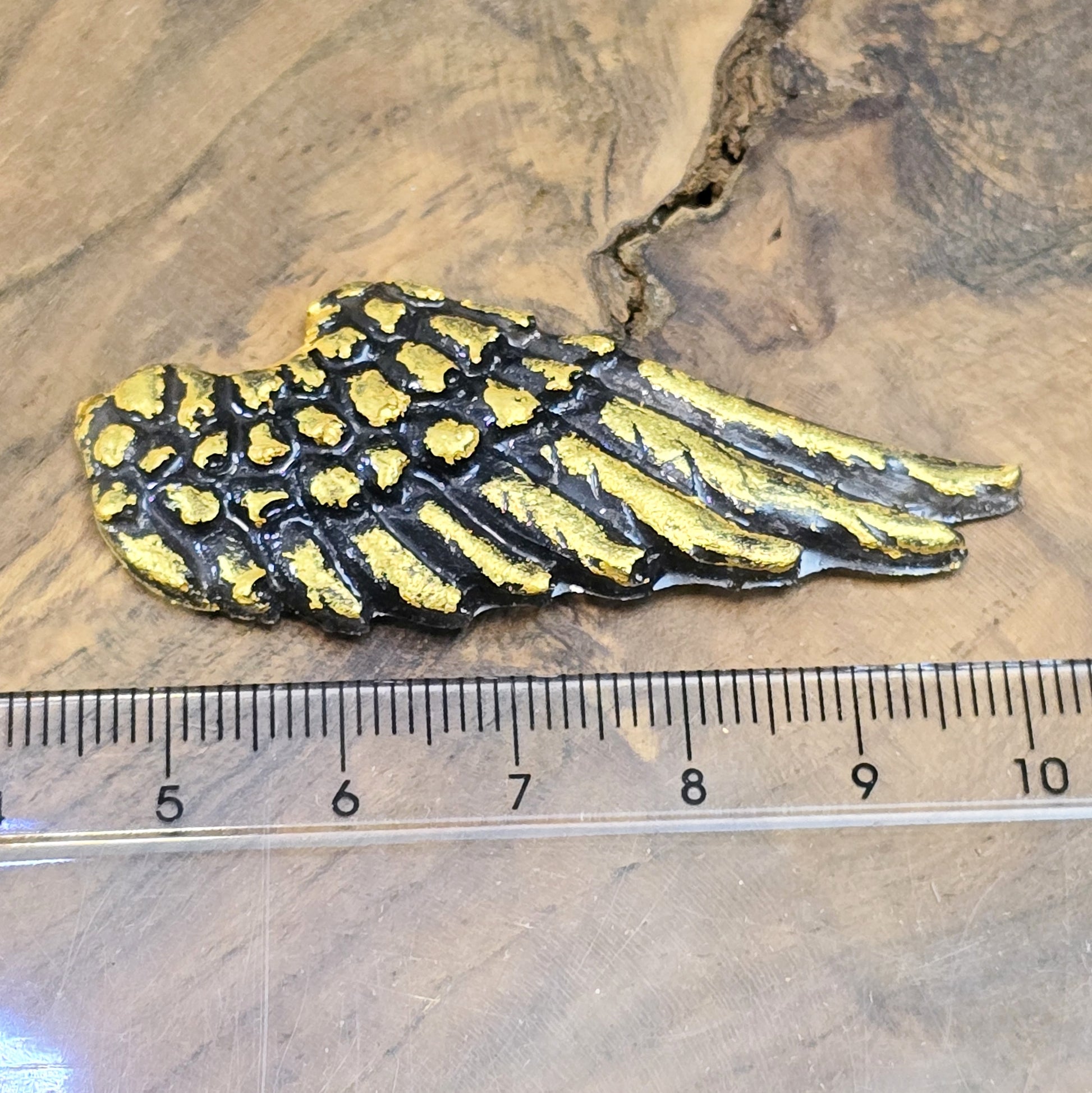 Auf dem Bild sind zwei handgefertigte Engelsflügel aus Kunstharz zu sehen. Die Flügel sind mit feinen, handbemalten Details verziert und haben eine flache Rückseite, die ideal für Schmuckherstellung oder Bastelprojekte geeignet ist.