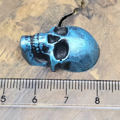 Das Bild zeigt einen Totenkopf-Cabochon in Schwarz mit türkisfarbener Wachsverzierung