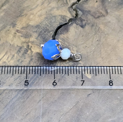 Das Bild zeigt zwei handgefertigte Anhänger mit einer blauen und einer weißen Kristallglasperle, ideal für die individuelle Schmuckherstellung.
