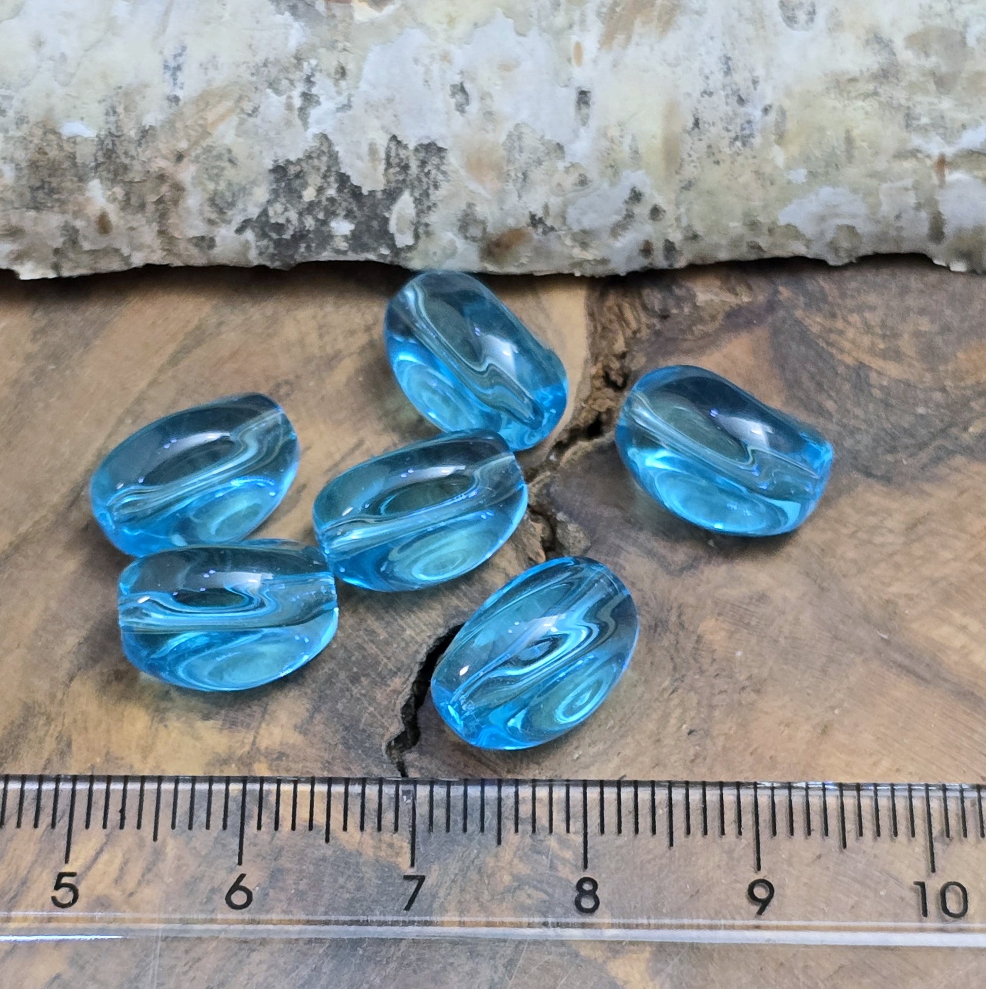 Das Bild zeigt 12 transparente Glasperlen in Nuggetform – Aquablau – 13mm – Für strahlend frische Schmuckkreationen