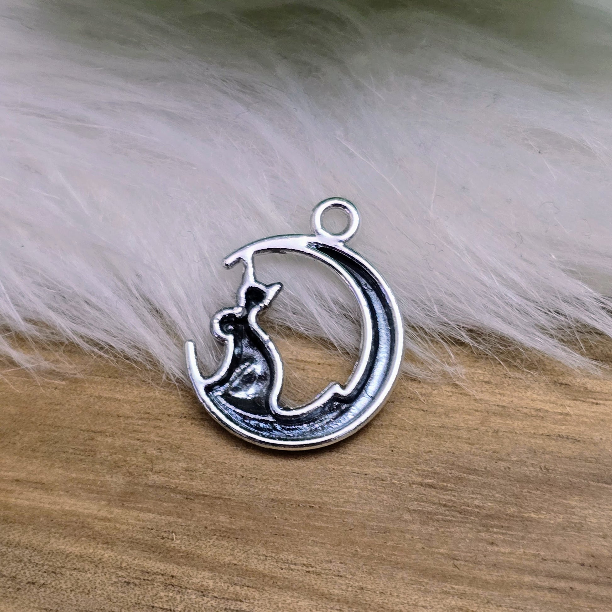 Das Bild zeigt einen Anhänger in Silberfarbe, der eine Katze im Mond darstellt. Die Katze ist elegant im Mond sitzend, begleitet von einem funkelnden rosé Strass-Stein. Der Anhänger ist ca. 20mm groß und eignet sich perfekt für die Schmuckherstellung oder als kreatives Accessoire.