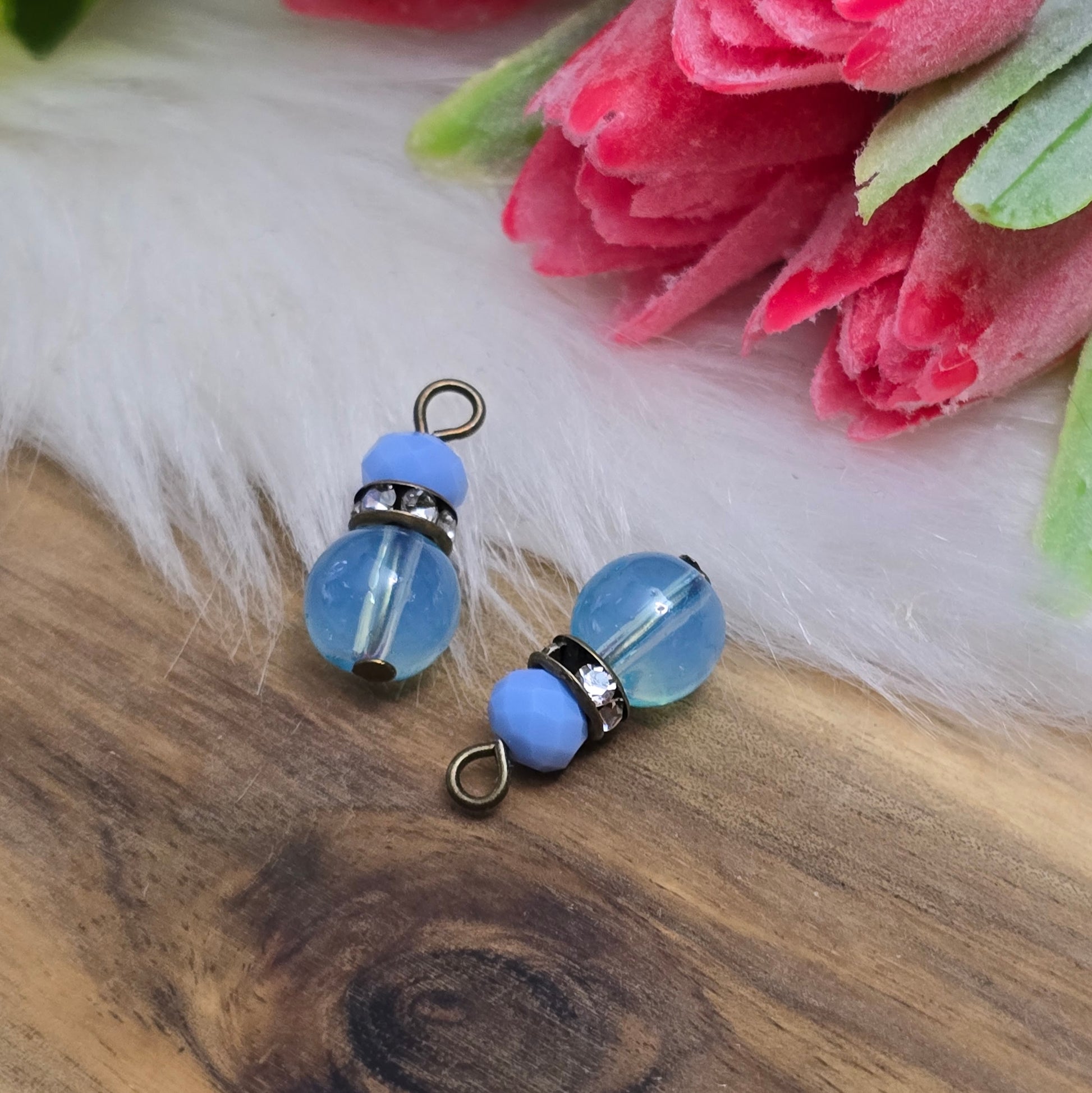 Das Bild zeigt zwei handgefertigte Anhänger mit einer Kombination aus transparenten hellblauen Glasperlen und opaken hellblauen Kristallglasperlen. Ein funkelndes Strassrondell setzt glitzernde Akzente, während antik bronzefarbige Metallelemente dem Design einen charmanten Vintage-Touch verleihen. Die filigranen Details und die harmonische Farbzusammenstellung machen die Anhänger zu einem stilvollen Blickfang für Schmuckkreationen.