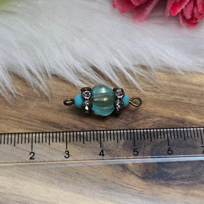 Das Bild zeigt zwei handgefertigte Verbinder mit mintfarbenen Glasperlen in Kürbisform und facettierten Kristallglasperlen. Strassrondelle sorgen für funkelnde Akzente, während antik bronzefarbene Metallelemente dem Design einen eleganten Vintage-Charme verleihen. Die Verbinder sind ca. 25mm groß und ideal für Schmuckkreationen.