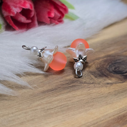 Das Bild zeigt zwei handgemachte Anhänger mit matten, orangefarbenen Glasperlen. Jedes Stück verfügt über ein elegantes, weißes Acrylblütenkäppchen, das einen verspielten Akzent setzt. Die antik silberfarbigen Perlenkappen runden das Design harmonisch ab. Mit einem Durchmesser von etwa 20mm sind die Anhänger filigran und ideal für Schmuckprojekte. Die Kombination aus lebendigen Farben und stilvollen Materialien verleiht den Anhängern einen attraktiven Look, der in jeder Schmuckkollektion hervorsticht.