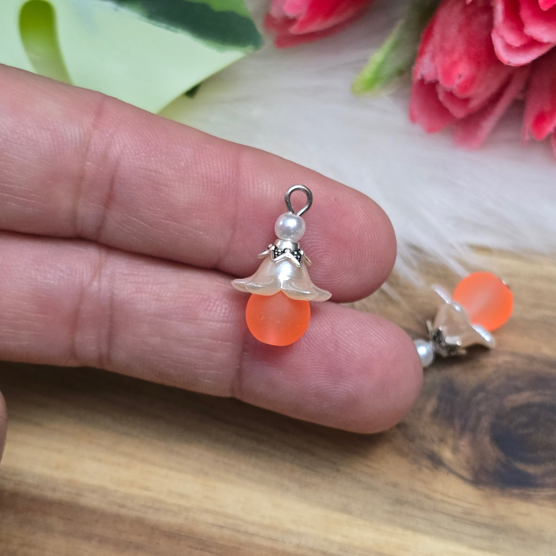 Das Bild zeigt zwei handgemachte Anhänger mit matten, orangefarbenen Glasperlen. Jedes Stück verfügt über ein elegantes, weißes Acrylblütenkäppchen, das einen verspielten Akzent setzt. Die antik silberfarbigen Perlenkappen runden das Design harmonisch ab. Mit einem Durchmesser von etwa 20mm sind die Anhänger filigran und ideal für Schmuckprojekte. Die Kombination aus lebendigen Farben und stilvollen Materialien verleiht den Anhängern einen attraktiven Look, der in jeder Schmuckkollektion hervorsticht.
