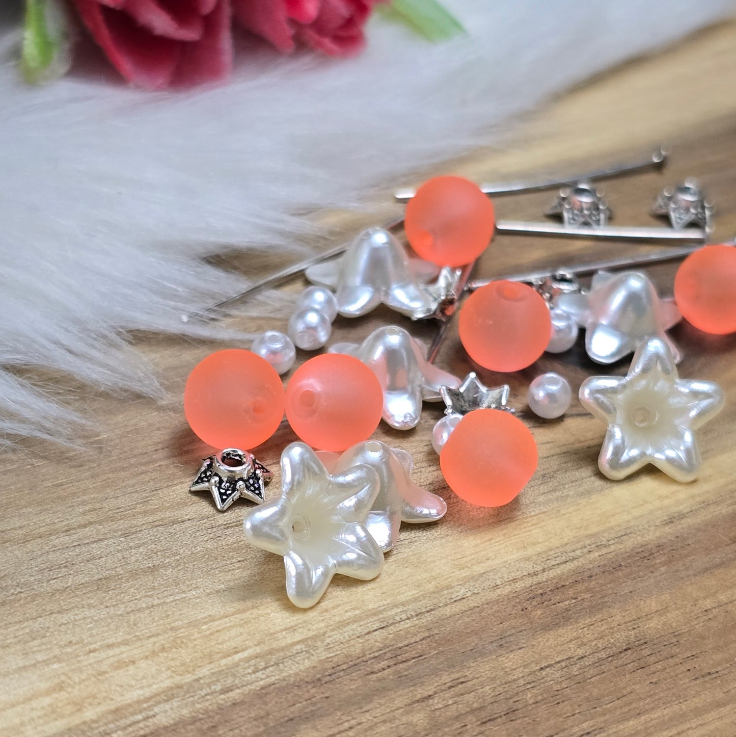 Das Bild zeigt ein 30-teiliges Bastelset zur Schmuckherstellung, ideal für kreative Bastler. In dem Set sind Materialien enthalten, um 6 Blumenanhänger in Orange und Weiß zu gestalten. Zu sehen sind verschiedene Komponenten: matte orangefarbene Glasperlen, cremeweiße Acrylperlen, weiße Blütenkäppchen und antik silberfarbige Sternkäppchen. Alle Teile sind sorgfältig angeordnet, um die Vielseitigkeit und Farbpalette des Sets hervorzuheben. Dieses Set bietet die perfekte Grundlage für die Gestaltung einzigarti