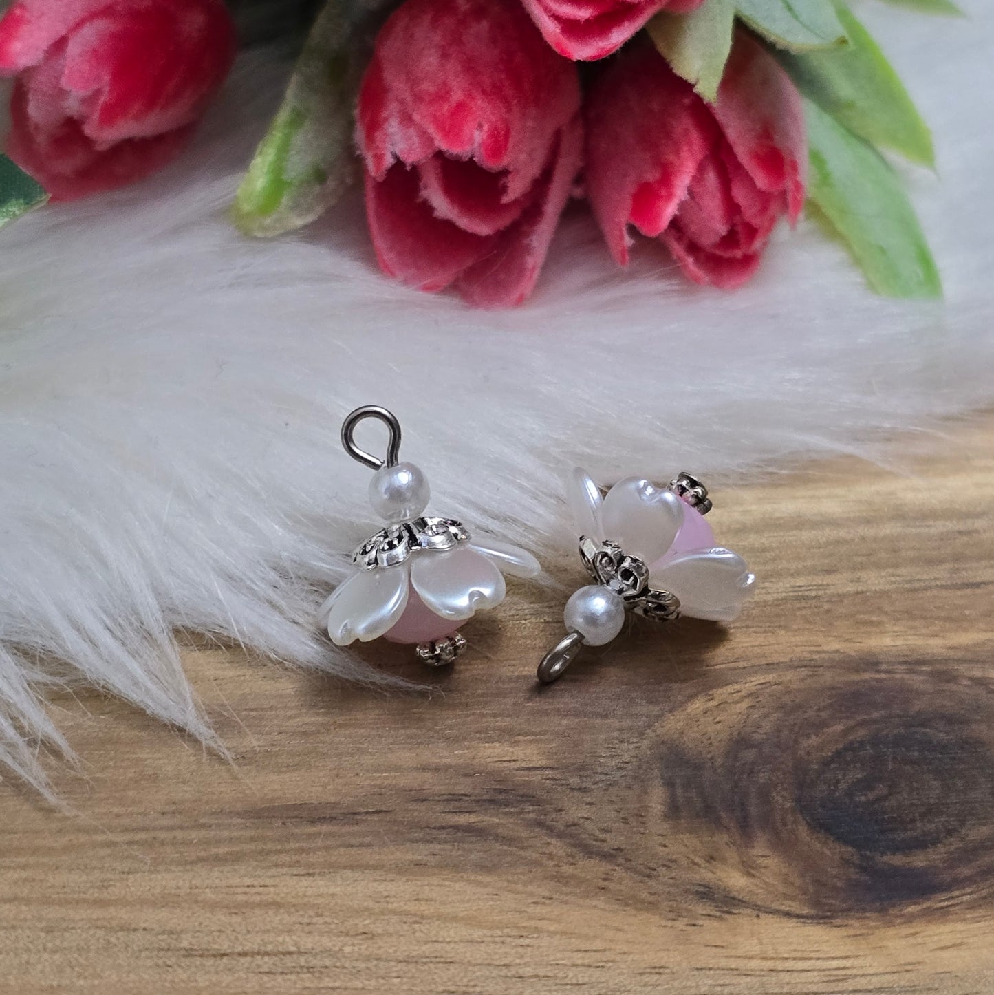 Auf dem Bild sind zwei handgefertigte Anhänger in Form von kleinen Blumen zu sehen. Die Anhänger bestehen aus einer eleganten weißen Acrylblüte und einer zarten rosafarbenen Kristallglasperle. Silberfarbige Metallelemente runden das Design ab und verleihen den Anhängern einen romantischen Charme. Mit einer Größe von ca. 18mm sind sie ideal für die individuelle Schmuckgestaltung, sei es für Ketten, Armbänder oder Ohrringe.