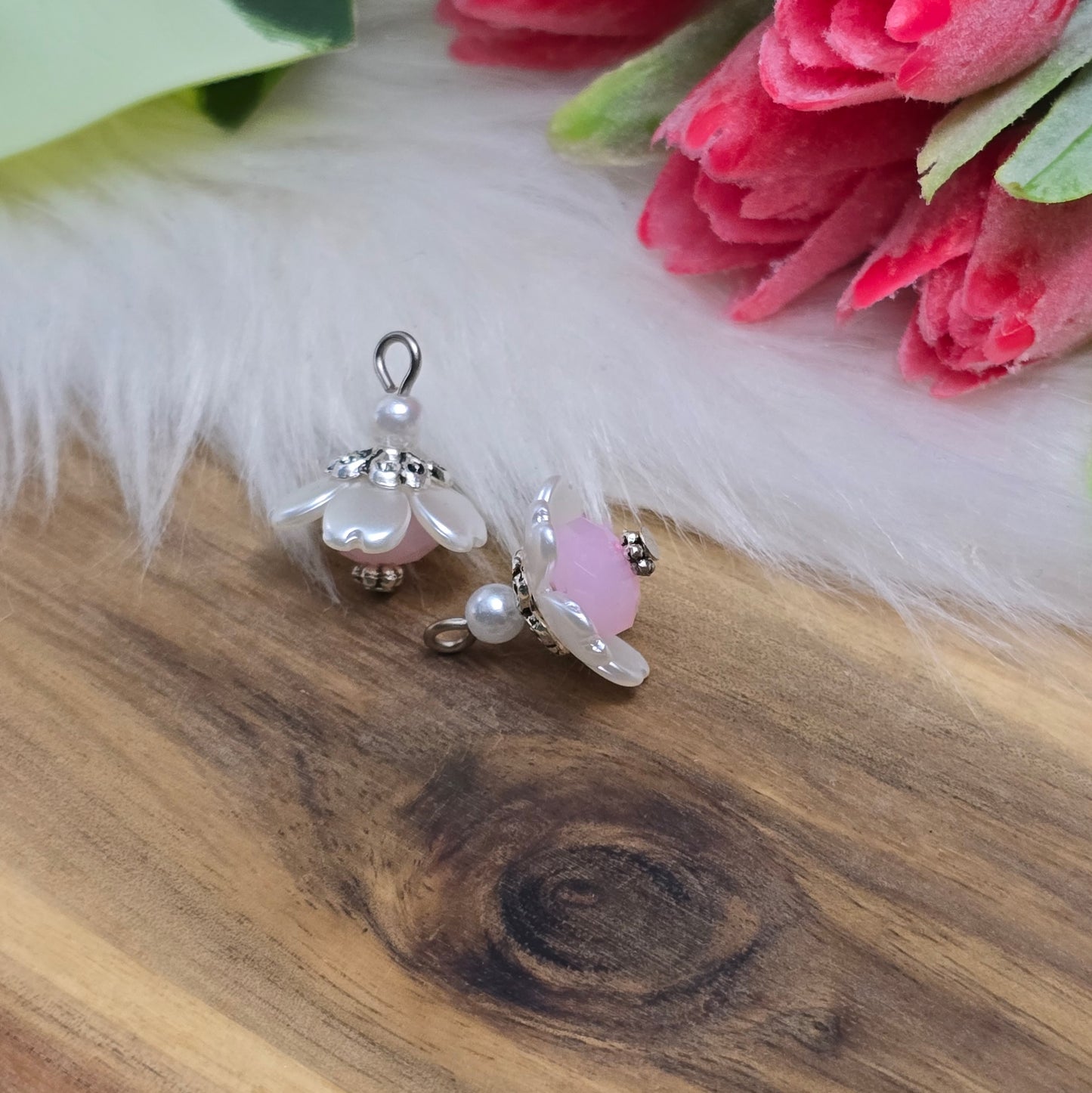 Auf dem Bild sind zwei handgefertigte Anhänger in Form von kleinen Blumen zu sehen. Die Anhänger bestehen aus einer eleganten weißen Acrylblüte und einer zarten rosafarbenen Kristallglasperle. Silberfarbige Metallelemente runden das Design ab und verleihen den Anhängern einen romantischen Charme. Mit einer Größe von ca. 18mm sind sie ideal für die individuelle Schmuckgestaltung, sei es für Ketten, Armbänder oder Ohrringe.
