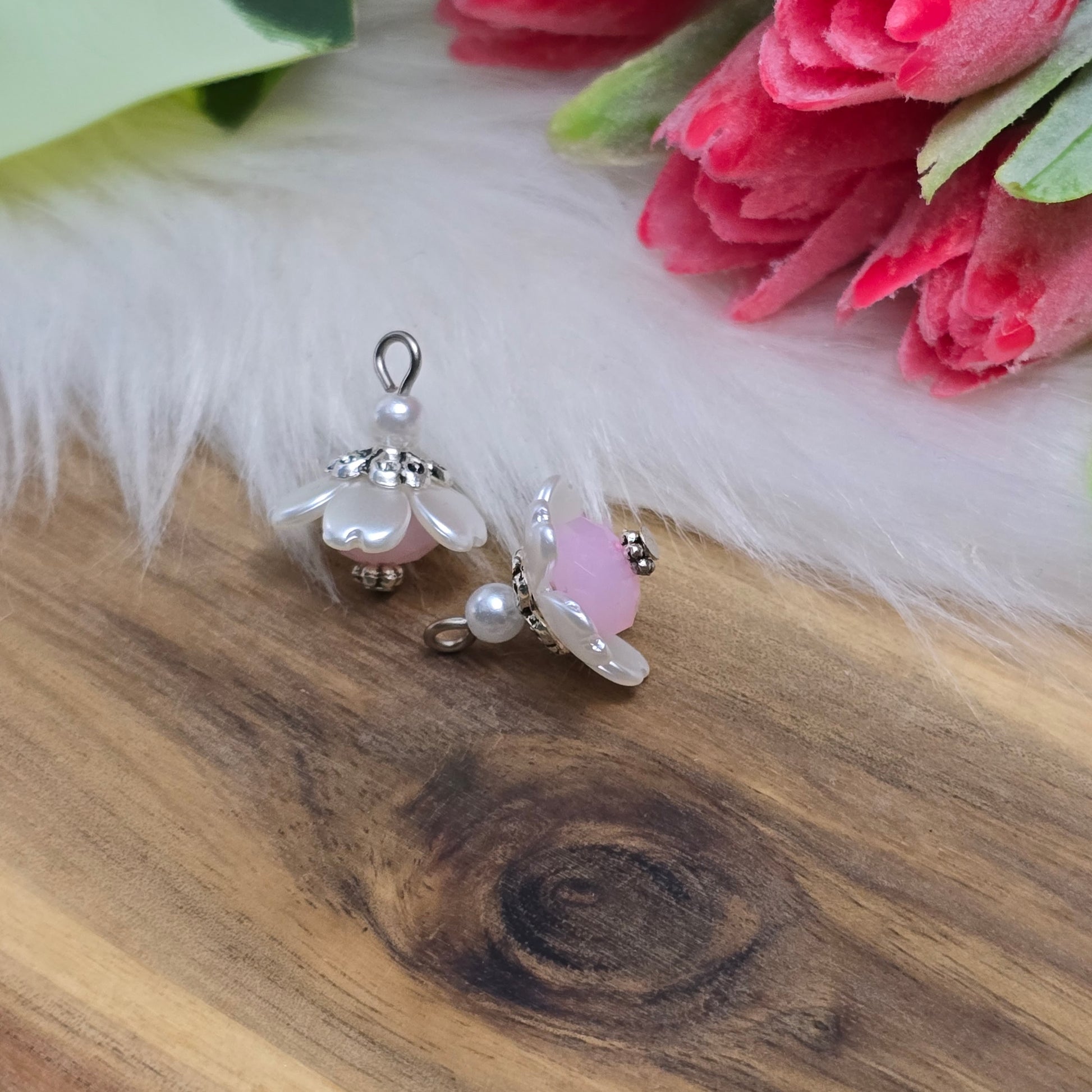 Auf dem Bild sind zwei handgefertigte Anhänger in Form von kleinen Blumen zu sehen. Die Anhänger bestehen aus einer eleganten weißen Acrylblüte und einer zarten rosafarbenen Kristallglasperle. Silberfarbige Metallelemente runden das Design ab und verleihen den Anhängern einen romantischen Charme. Mit einer Größe von ca. 18mm sind sie ideal für die individuelle Schmuckgestaltung, sei es für Ketten, Armbänder oder Ohrringe.