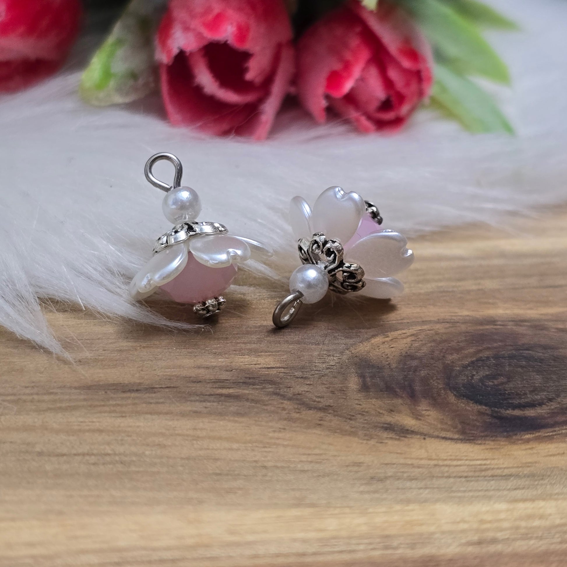Auf dem Bild sind zwei handgefertigte Anhänger in Form von kleinen Blumen zu sehen. Die Anhänger bestehen aus einer eleganten weißen Acrylblüte und einer zarten rosafarbenen Kristallglasperle. Silberfarbige Metallelemente runden das Design ab und verleihen den Anhängern einen romantischen Charme. Mit einer Größe von ca. 18mm sind sie ideal für die individuelle Schmuckgestaltung, sei es für Ketten, Armbänder oder Ohrringe.