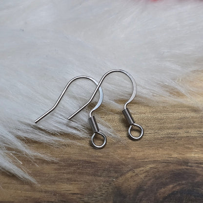 Das Bild zeigt ein Paar French Ohrhaken aus 304 Edelstahl in Silberfarbe. Die Haken haben eine elegante, geschwungene Form mit einer kleinen Öse am unteren Ende, die zur Befestigung von Anhängern oder Perlen dient. Die Oberfläche ist glatt und glänzend, was ihnen ein hochwertiges und modernes Aussehen verleiht. Mit einer Größe von etwa 16 mm sind sie ideal für die Gestaltung individueller Ohrringe.