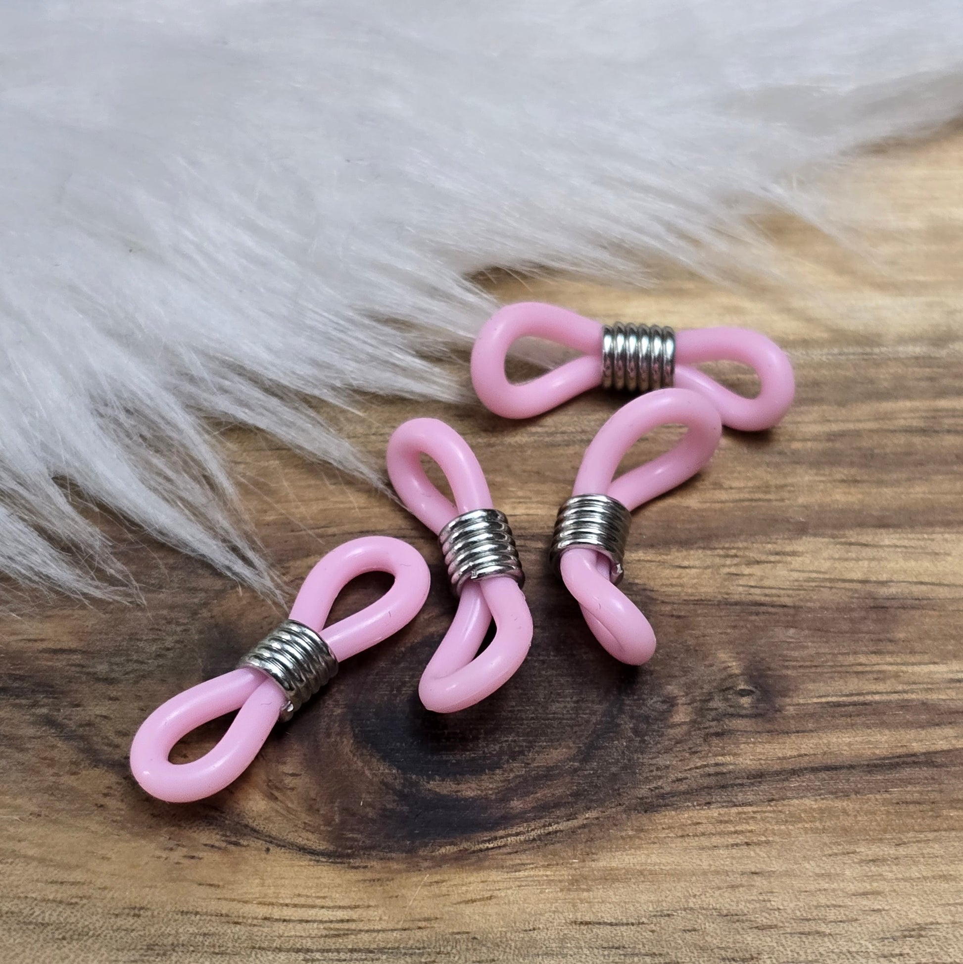Das Bild zeigt eine Auswahl an Silikonschlaufen für Brillenketten und Maskenhalter in drei Farben: Mint, Rosa und Schwarz. Jede Schlaufe hat eine flexible, weiche Textur und ist so gestaltet, dass sie einfach auf den Bügel der Brille geschoben werden kann. An einem Ende der Schlaufe befindet sich ein kleiner Metallring, der fest angebracht ist, um ein Abrutschen zu verhindern. Die anderen Enden der Schlaufen sind offen, sodass sie mit einem Karabiner oder Biegering leicht an einer Kette befestigt werden kön