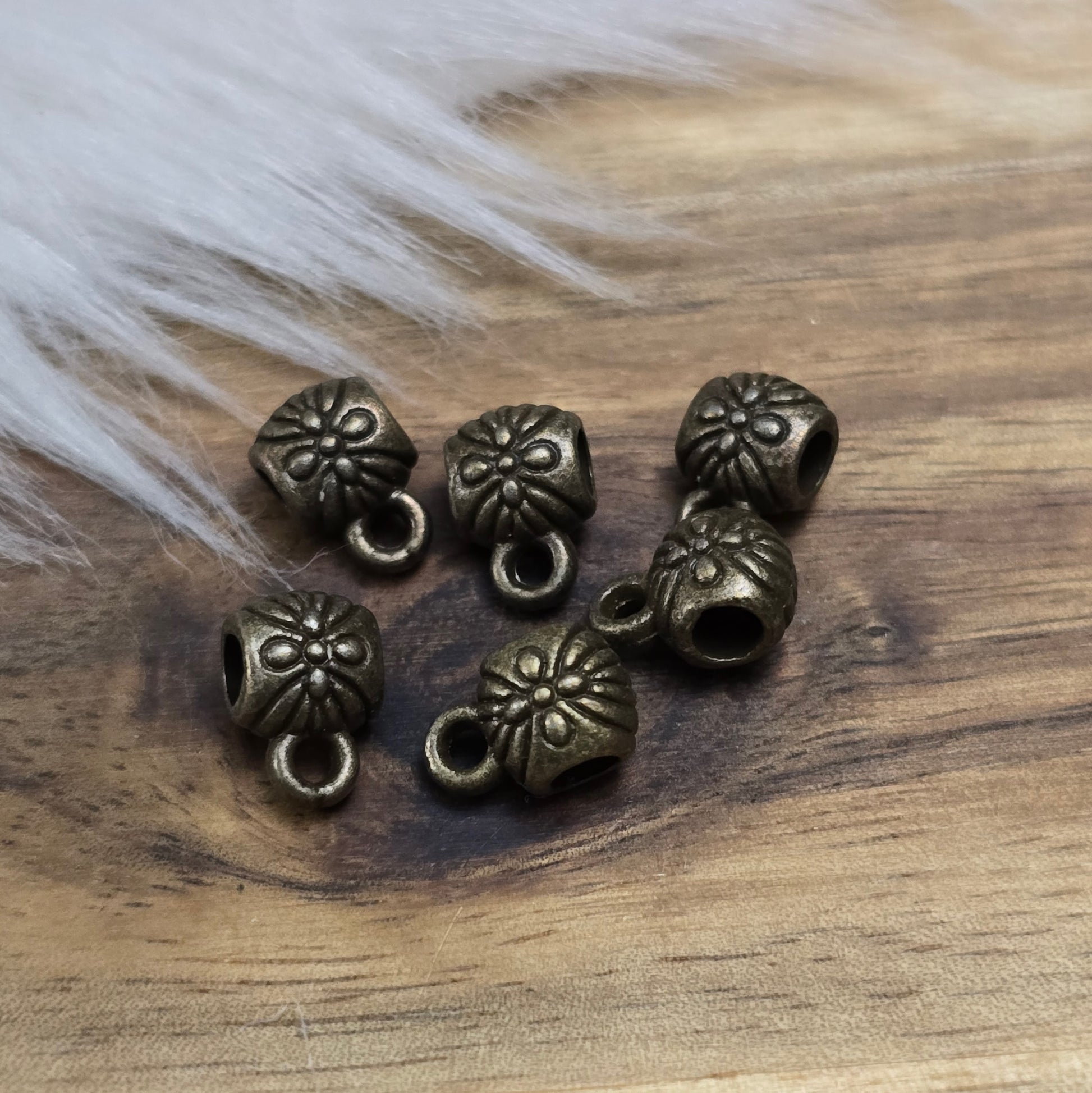 Das Bild zeigt ein Set von 6 antik bronzefarbenen Metallperlen mit Anhängerösen, die einen Durchmesser von etwa 6 mm haben. Jede Perle ist mit einer praktischen Anhängeröse ausgestattet, die es ermöglicht, sie leicht an Ketten oder Armbändern zu befestigen. Die Metallperlen besitzen ein großzügiges Fädelloch, das das Einfädeln von Schnüren oder Drähten erleichtert. Ihr antik bronzefarbiges Finish verleiht ihnen eine elegante und zeitlose Ästhetik, die sich ideal für die Herstellung individueller Schmuckstüc