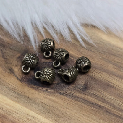 Das Bild zeigt ein Set von 6 antik bronzefarbenen Metallperlen mit Anhängerösen, die einen Durchmesser von etwa 6 mm haben. Jede Perle ist mit einer praktischen Anhängeröse ausgestattet, die es ermöglicht, sie leicht an Ketten oder Armbändern zu befestigen. Die Metallperlen besitzen ein großzügiges Fädelloch, das das Einfädeln von Schnüren oder Drähten erleichtert. Ihr antik bronzefarbiges Finish verleiht ihnen eine elegante und zeitlose Ästhetik, die sich ideal für die Herstellung individueller Schmuckstüc