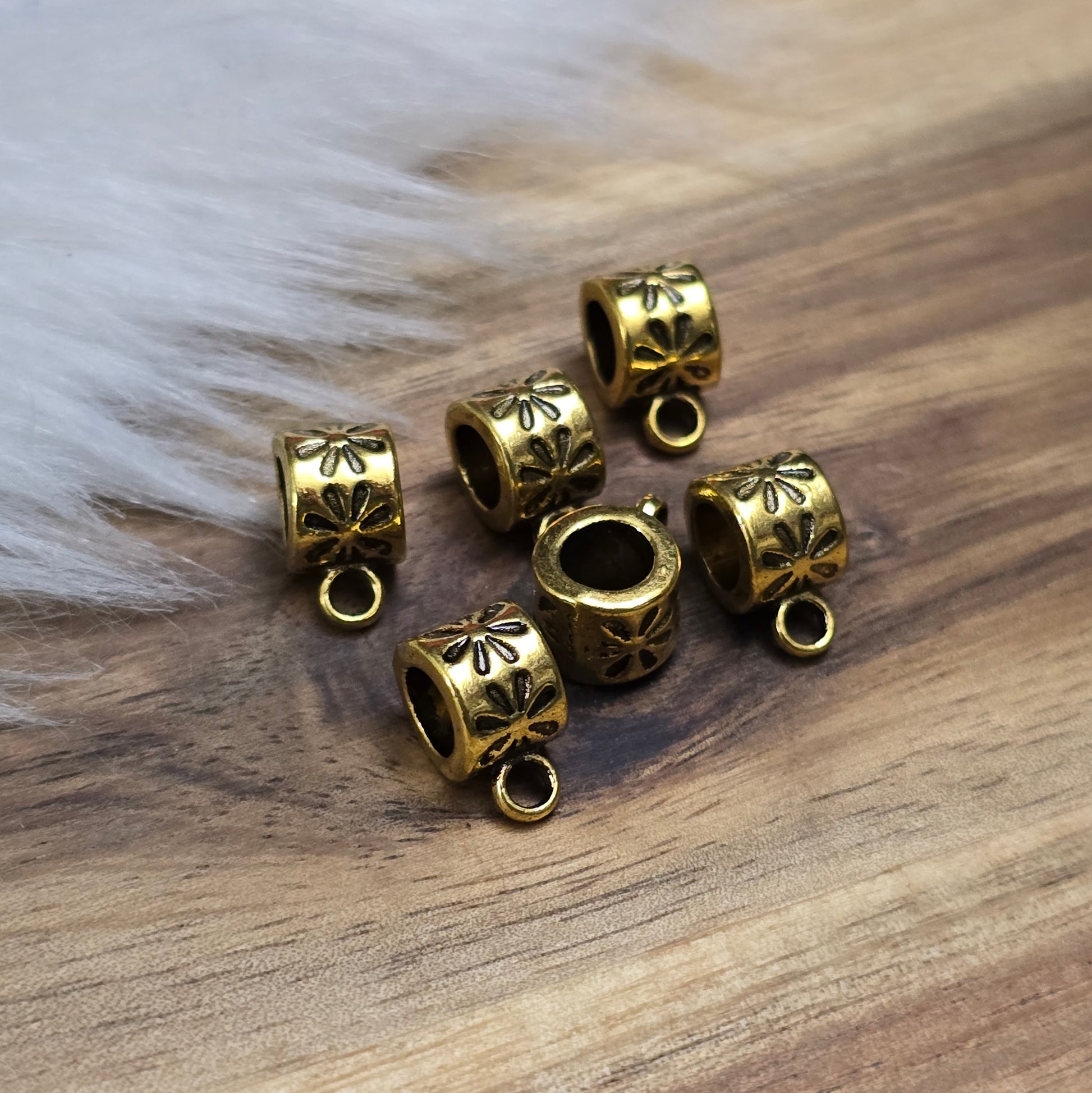 Das Bild zeigt 12 antik goldfarbene Metallperlen mit integrierter Anhängeröse. Die runden Perlen haben eine glatte Oberfläche und eine Öffnung zum einfachen Auffädeln auf Ketten oder Armbänder. Die fest angebrachte Öse ermöglicht das Befestigen von Anhängern für individuelle Schmuckdesigns.