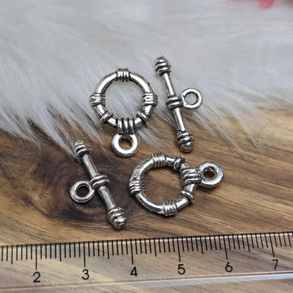 Die Abbildung zeigt zwei antik silberfarbene Knebelverschlüsse, bestehend aus einem Ring und einem Stab. Diese hochwertigen Verschlüsse bieten eine elegante Lösung für Schmuckstücke wie Armbänder und Ketten. Ihr klassisches Design verleiht jedem Projekt eine dekorative Note und sorgt gleichzeitig für eine sichere Verschlussmöglichkeit.
