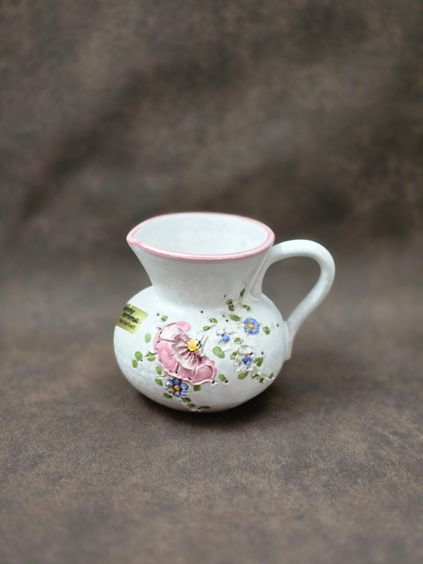 Handgefertigter Vintage-Dekokrug aus Ainring Keramik mit floralem Relief, matter Glasur und Originalaufkleber, deutsche Kunstkeramik der 1960er–1970er Jahre.