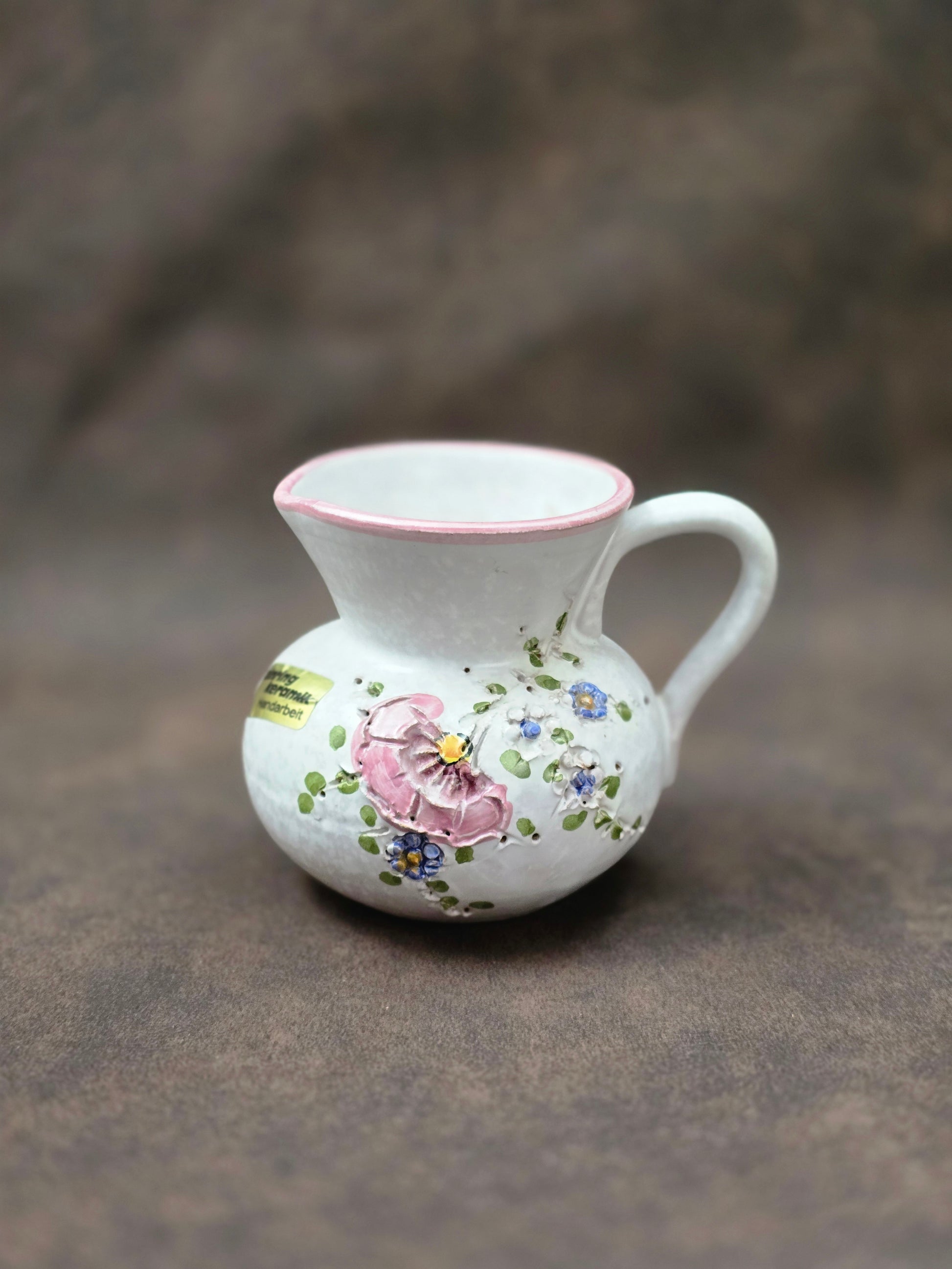 Handgefertigter Vintage-Dekokrug aus Ainring Keramik mit floralem Relief, matter Glasur und Originalaufkleber, deutsche Kunstkeramik der 1960er–1970er Jahre.